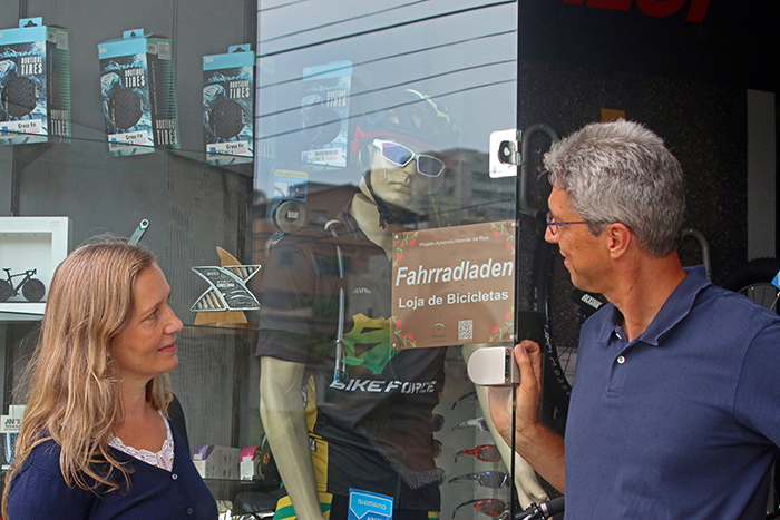 Professores de alemão instalam placas bilíngues em estabelecimentos comerciais da Cidade Alta 1 Por uma via alemã: Alexandre e a esposa Christine exibem placa fixada em loja de bicicletas (Foto: Leonardo Costa)