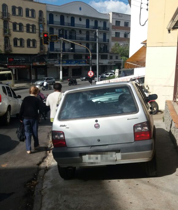 Carro toma todo o espaço da calçada e força pedestres a andarem pela rua.