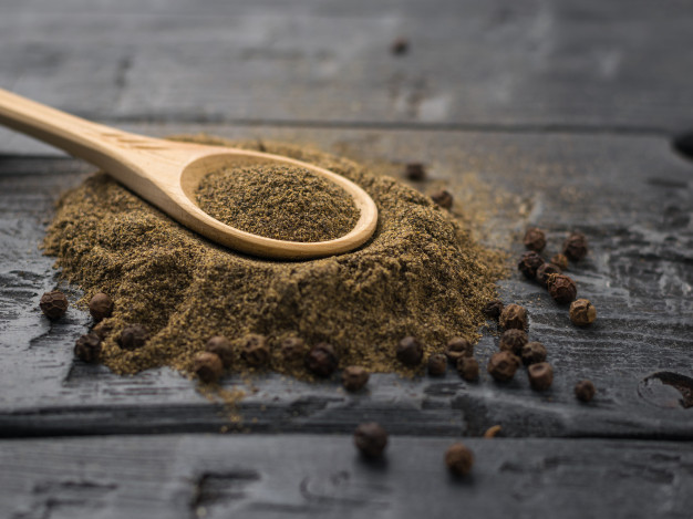 Utilize os temperos para turbinar a sua saúde 9 uma colher de pau com pimenta do reino moida em uma pilha de pimenta inteira em uma mesa escura rustica 94064 1583