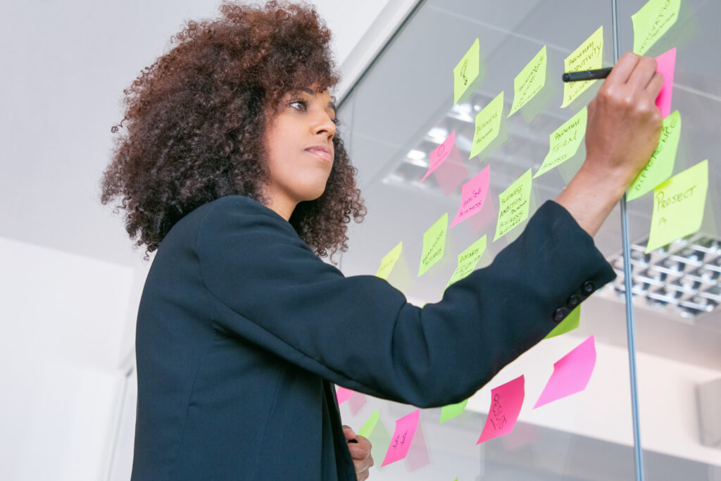 Produtividade: como o planejamento e a priorização são importantes aliados neste processo 2 successful pretty businesswoman writing sticker with marker thoughtful confident curly female manager sharing idea project making note brainstorming business training concept
