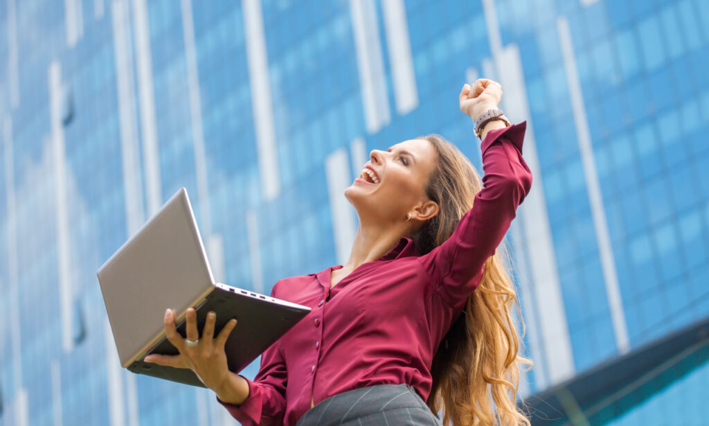 Como e porque desenvolver a resiliência profissional? 2 empresaria e a vencedora do acordo entre empresas da cidade mulher de cabelo comprido e a profissional ela esta segurando laptop e rindo muito
