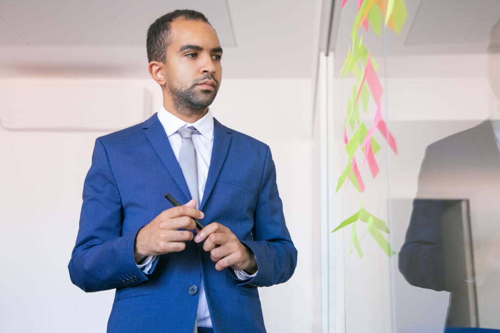 Carreira pós-IA: como se tornar um profissional insubstituível 2 african american office employer holding pen reading notes glass wall focused confident businessman suit thinking about idea project