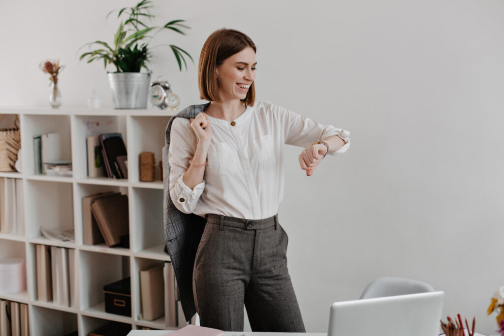 Como os hábitos moldam carreiras sem que percebamos 1 laughing business woman white blouse gray pants is looking wrist watch standing against office furniture