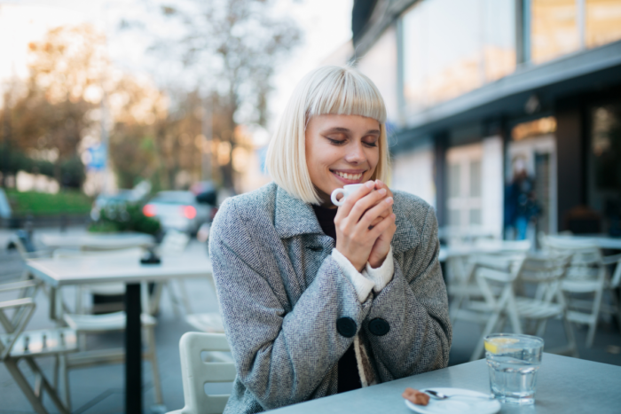 Mulher tomando café com um sorriso e segurando a xícara com carinho