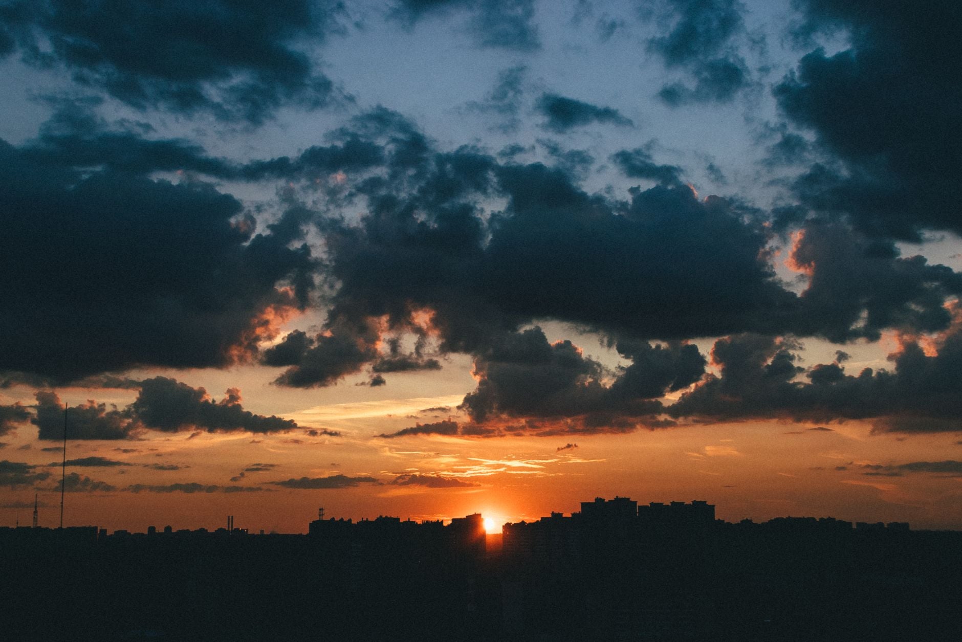 Um pôr do sol espetacular com a silhueta da cidade recortada e nuvens vibrantes.