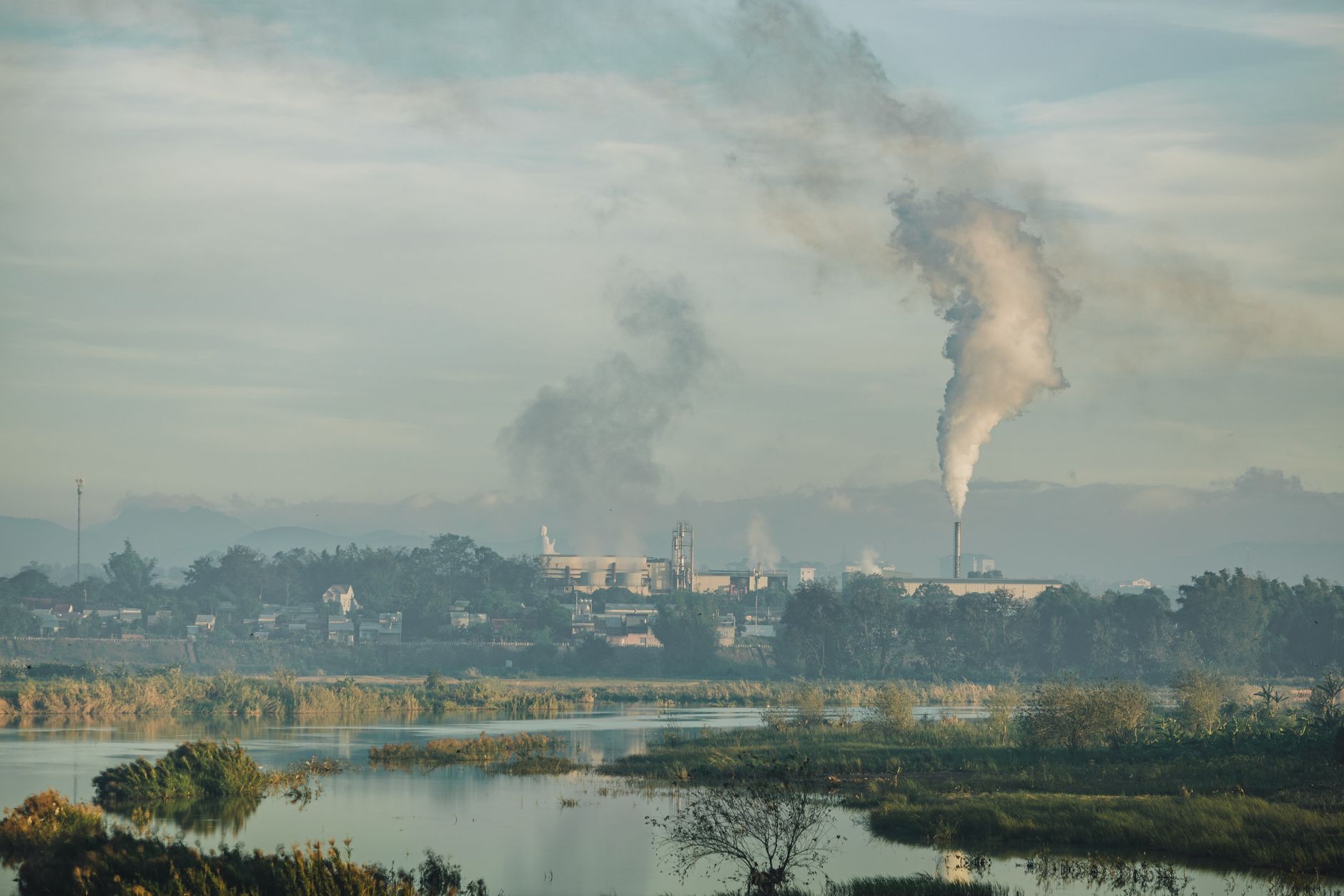 Uma fábrica emitindo fumaça sobre uma paisagem natural em Kon Tum, no Vietnã.
