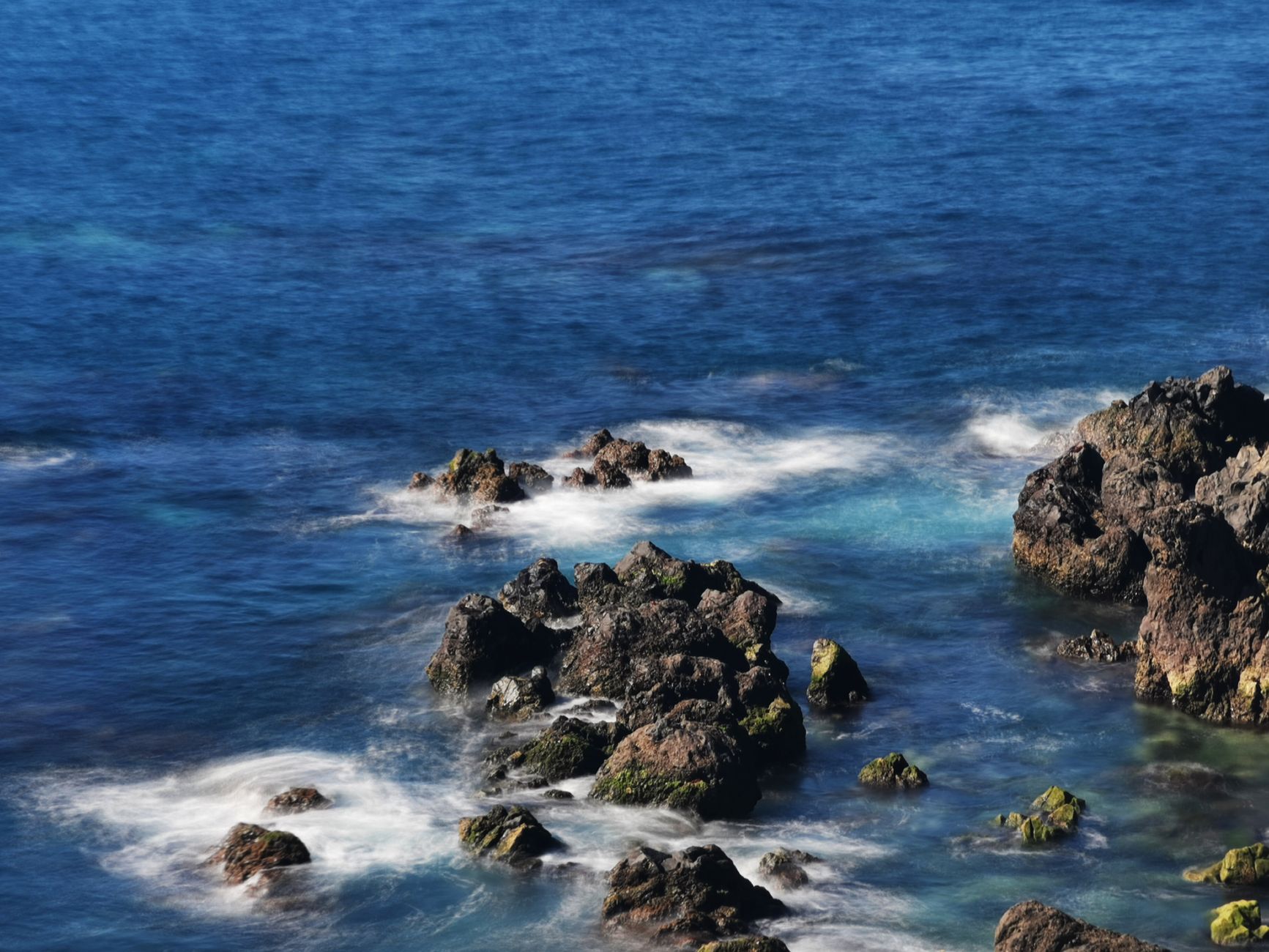 China faz alerta para fenômeno histórico entre os maiores já registrados que está se formando e pode afetar o mundo inteiro 1 Vista dramática de rochas erodidas iluminadas pelo sol ao longo da costa, cercadas por um mar azul profundo.