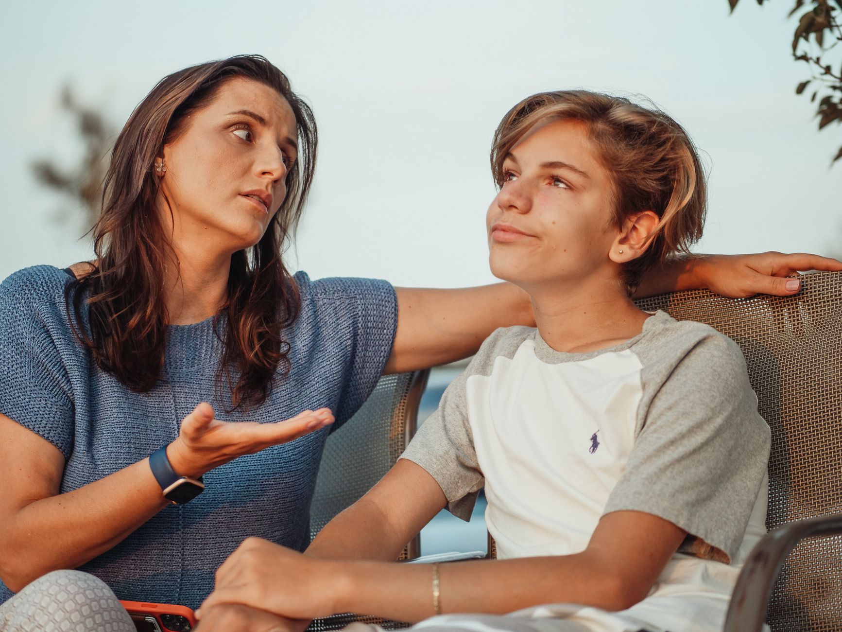 Em vez de dar a resposta quando o filho enfrenta um problema, psiquiatra recomenda fazer duas perguntas que estimulam a criança a encontrar a própria solução 1 Uma mãe e seu filho adolescente conversam do lado de fora, expressando calor e conexão familiar.