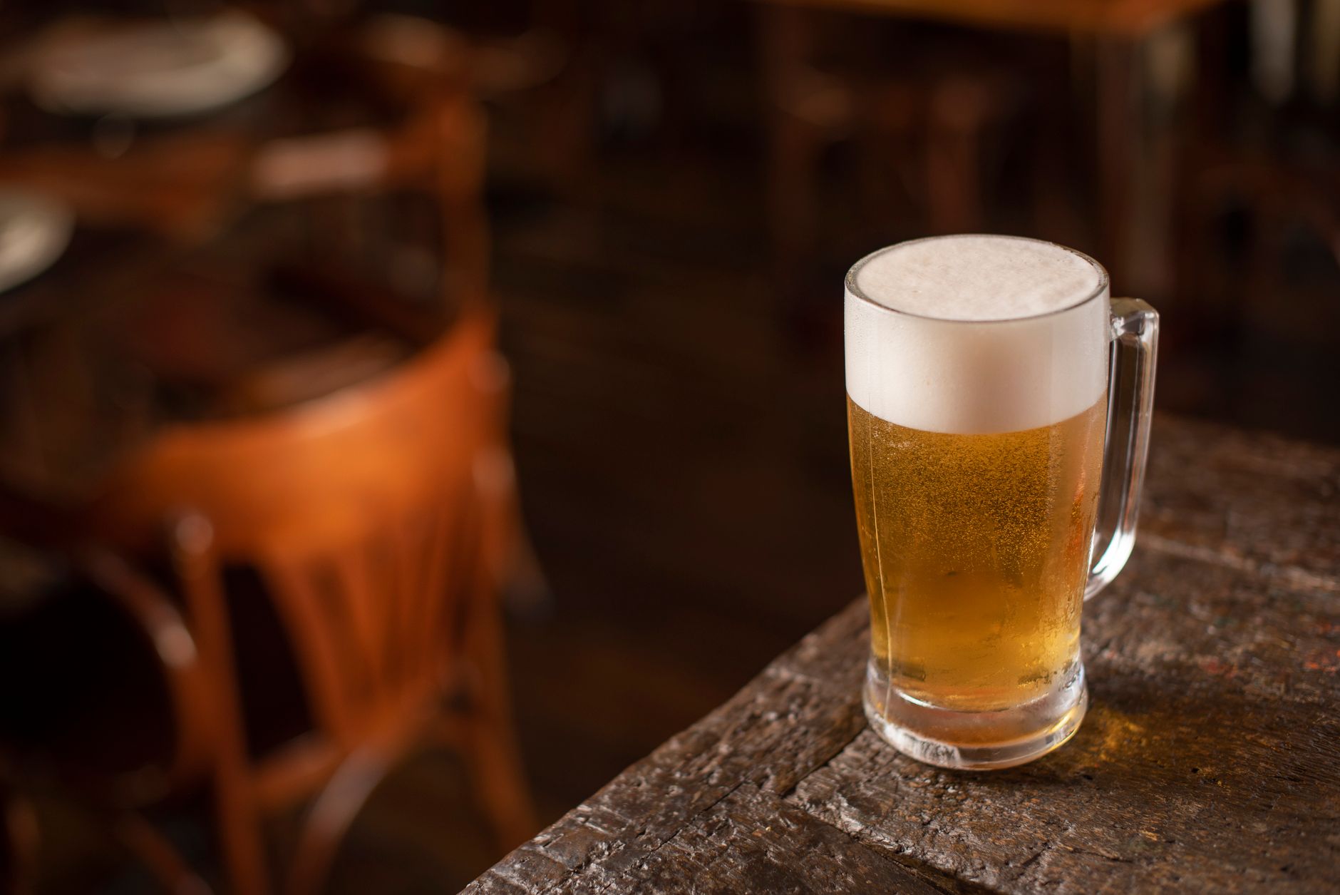 Enquanto moradores de alguns estados terão que passar parte do domingo sem comprar ou consumir bebidas alcoólicas, outros poderão frequentar bares normalmente durante o primeiro turno das eleições 1 Close-up de uma caneca de cerveja espumante em uma mesa de madeira em um ambiente aconchegante de pub.