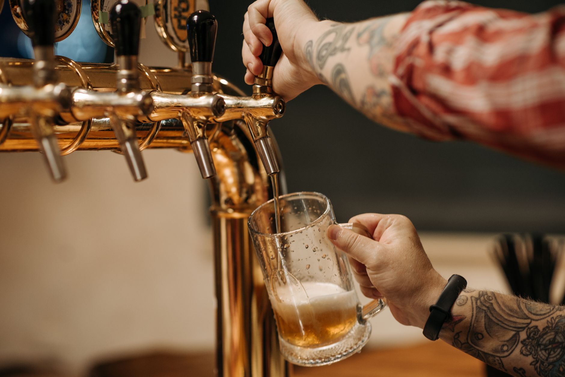 Enquanto moradores de alguns estados terão que passar parte do domingo sem comprar ou consumir bebidas alcoólicas, outros poderão frequentar bares normalmente durante o primeiro turno das eleições 4 Bartender tatuado servindo uma pint de cerveja de uma torneira dourada, vista em close em um bar.