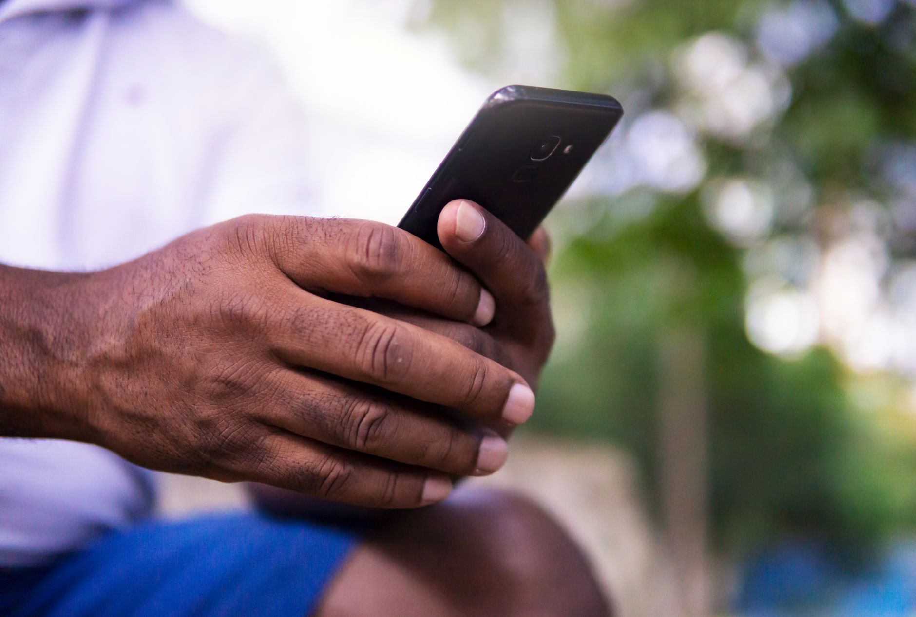 Especialista revela quantas vezes você realmente deve lavar as mãos durante o dia e aponta o lugar da casa que concentra mais germes 2 Um close das mãos de um homem segurando um smartphone em um parque, mostrando o uso da tecnologia.