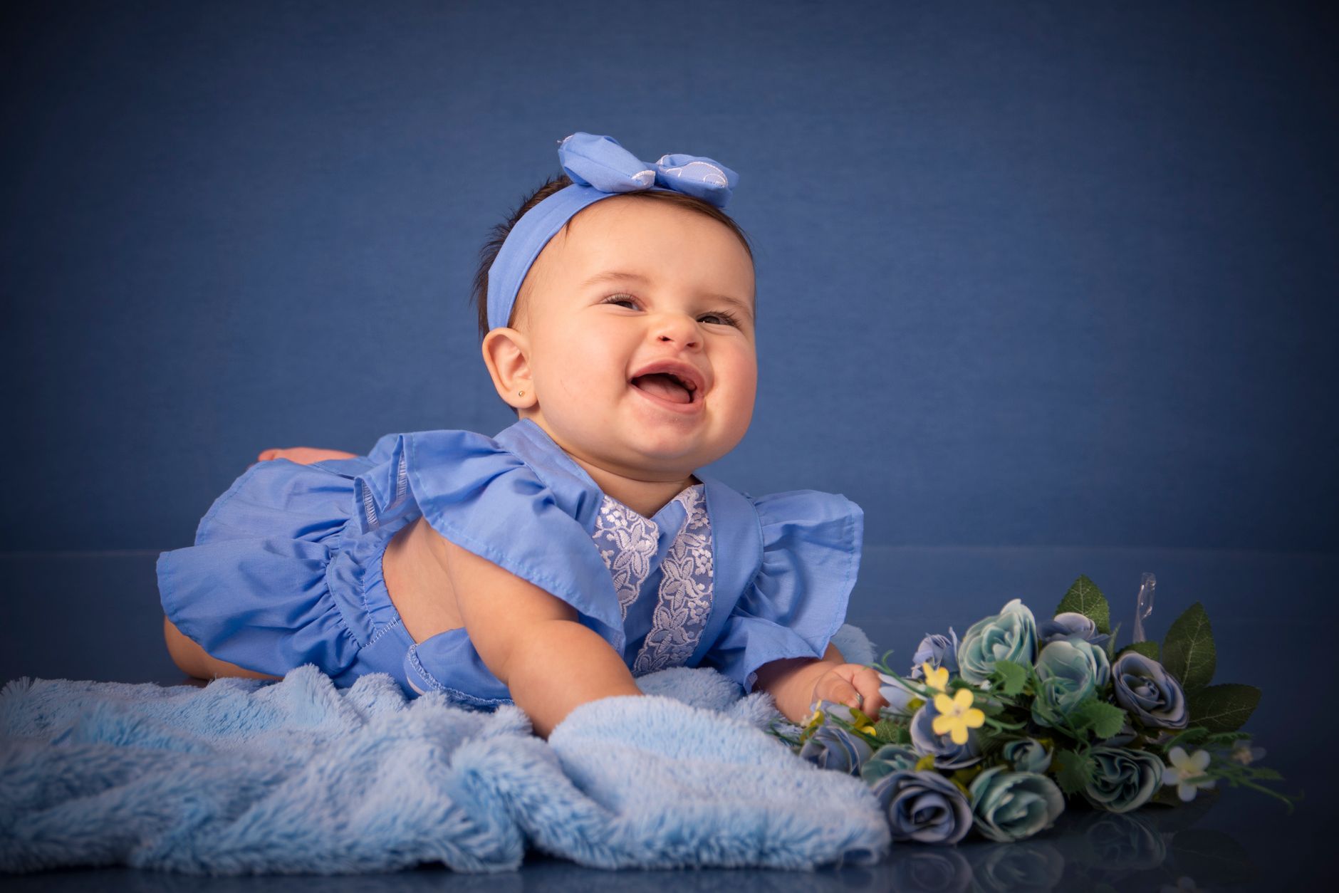 Esses nomes de bebê mais populares dos anos 2000 ainda reinam mesmo depois de 20 Anos 1 Bebê encantador com roupa azul e faixa na cabeça, sorrindo em um fundo azul com flores.