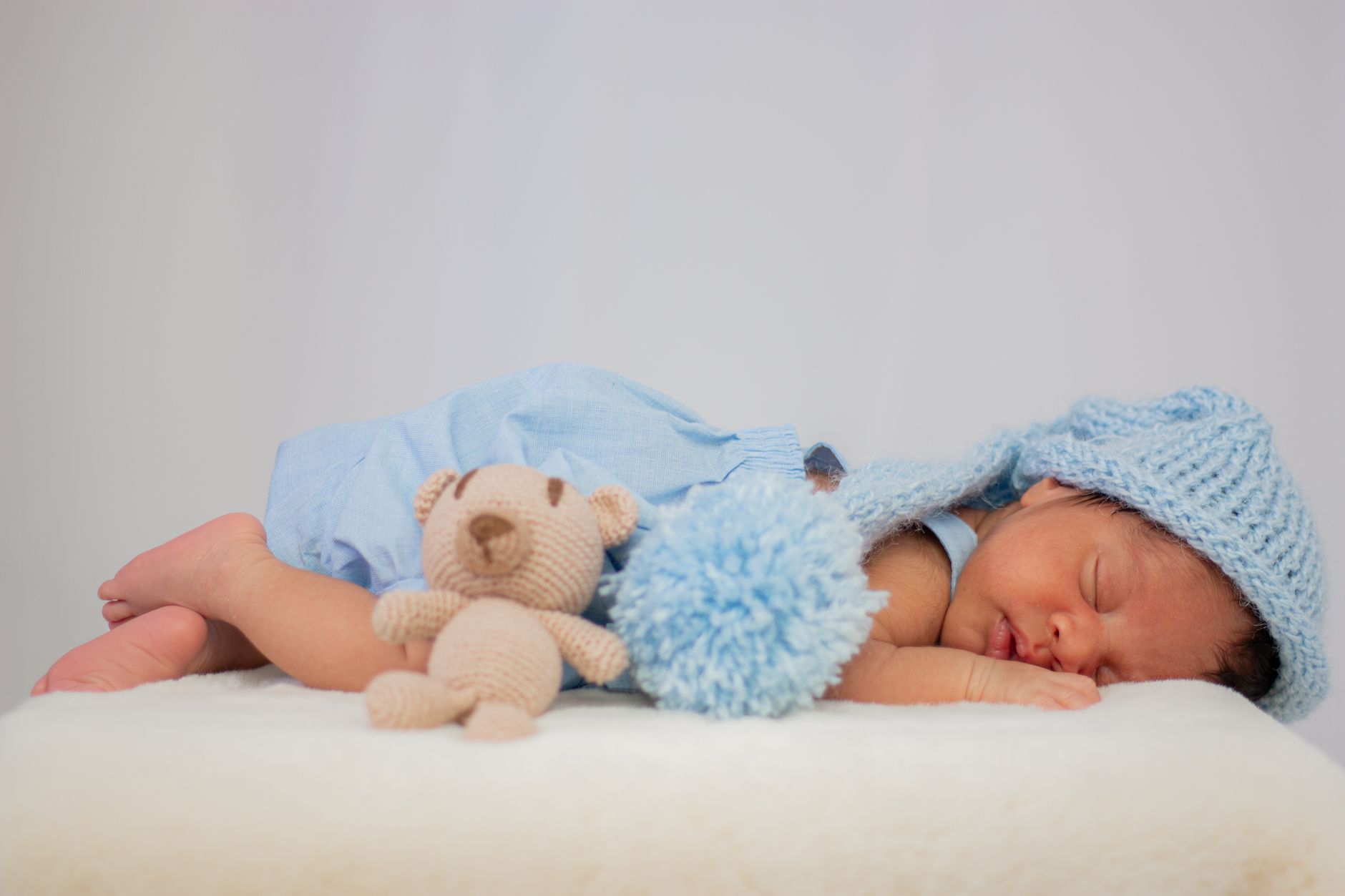 Esses nomes de bebê mais populares dos anos 2000 ainda reinam mesmo depois de 20 Anos 2 Uma imagem serena de um recém-nascido dormindo em um traje azul, adornado com um adorável urso de pelúcia.