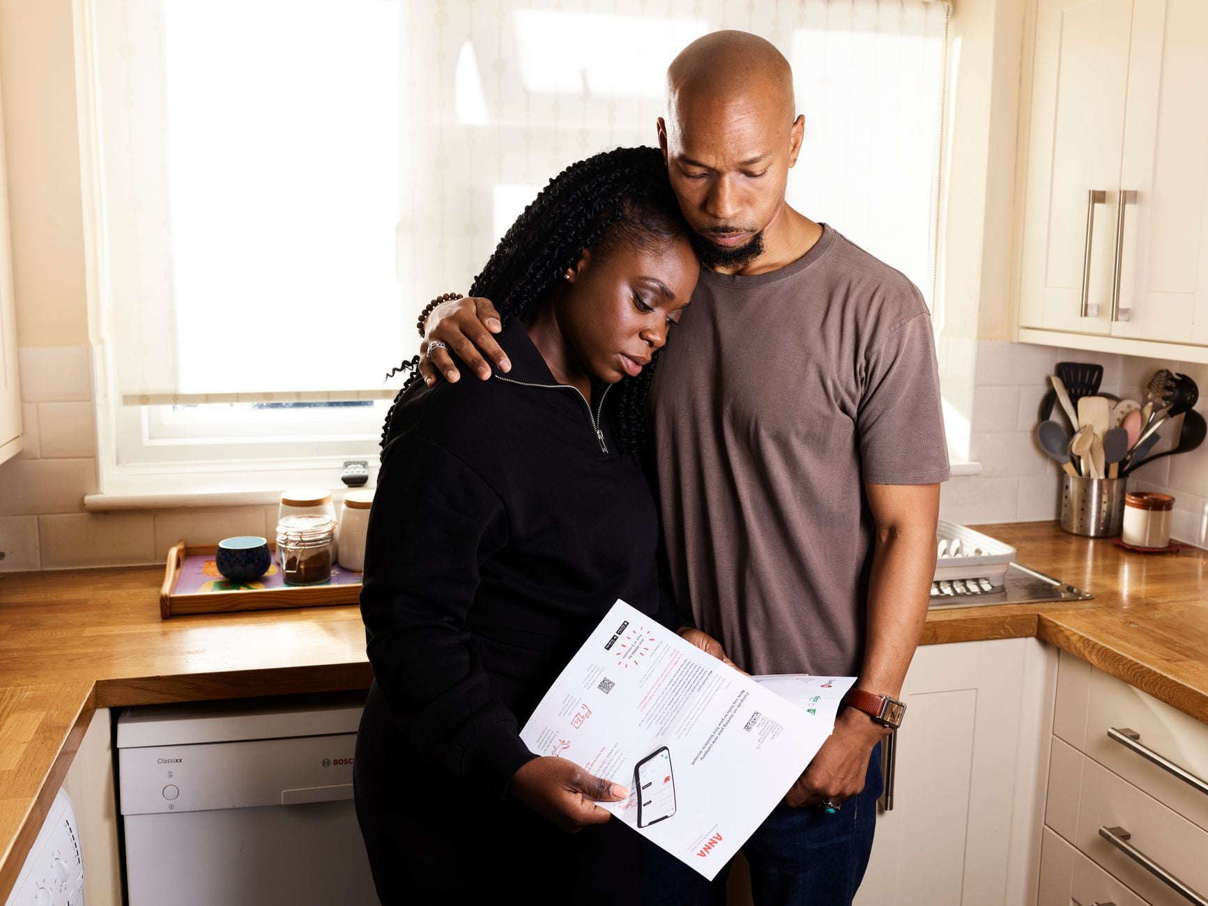 “Eu deveria ter feito isso antes”: pessoas com mais de 30 anos compartilham arrependimentos e conselhos que gostariam de ter recebido quando eram mais jovens 2 Um casal se abraça na cozinha enquanto revisam documentos importantes, refletindo preocupação e apoio.