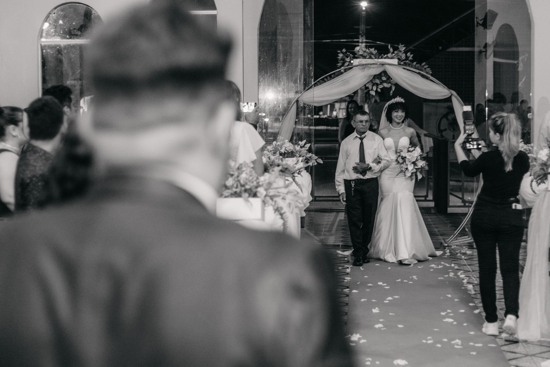Filho decide não ir à festa de casamento do pai por causa de um compromisso de última hora e atitude acaba gerando uma discussão familiar 1 Pai acompanha a noiva sorridente pelo corredor em cerimônia de casamento interna. Capturado em preto e branco.