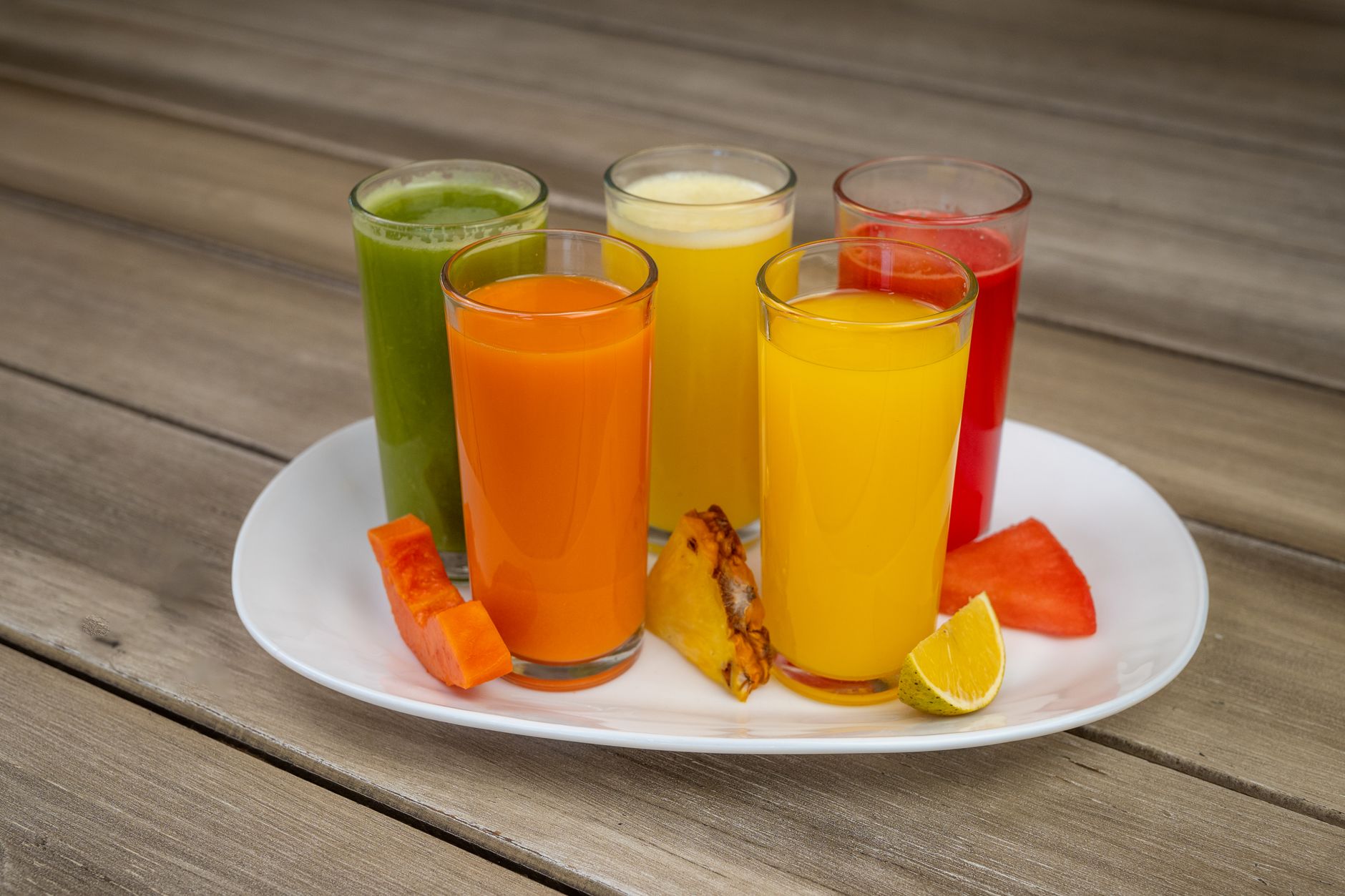 Fruta pode fazer bem ao coração, mas estudo com 371 mil pessoas encontrou um detalhe que muda a forma como muita gente consome esse alimento no dia a dia 2 Variedade colorida de sucos de frutas frescas em copos sobre um prato branco com frutas variadas.