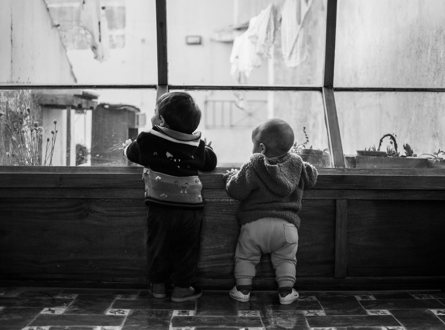 Nasceu nos anos 60, 70, 80 ou 90? Lista revela os nomes que mais fizeram sucesso entre os bebês de cada década 2 Dois bebês estão em pé dentro de casa olhando pela janela em uma fotografia em preto e branco.