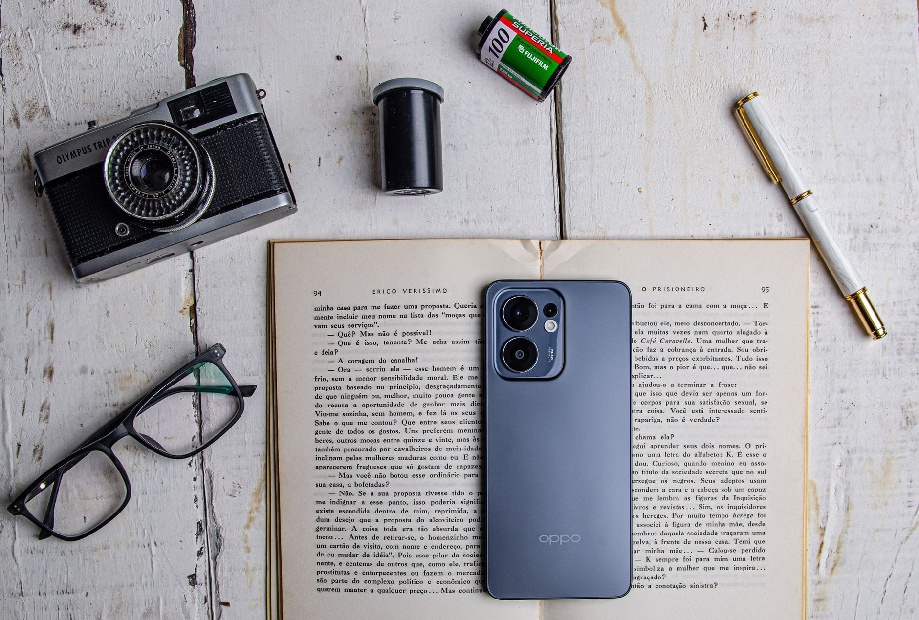 O jeito certo de deixar o celular na mesa pode ajudar a evitar distrações e esconder suas notificações de quem está por perto 1 Uma visão de cima de uma câmera vintage, smartphone e acessórios em um livro aberto.
