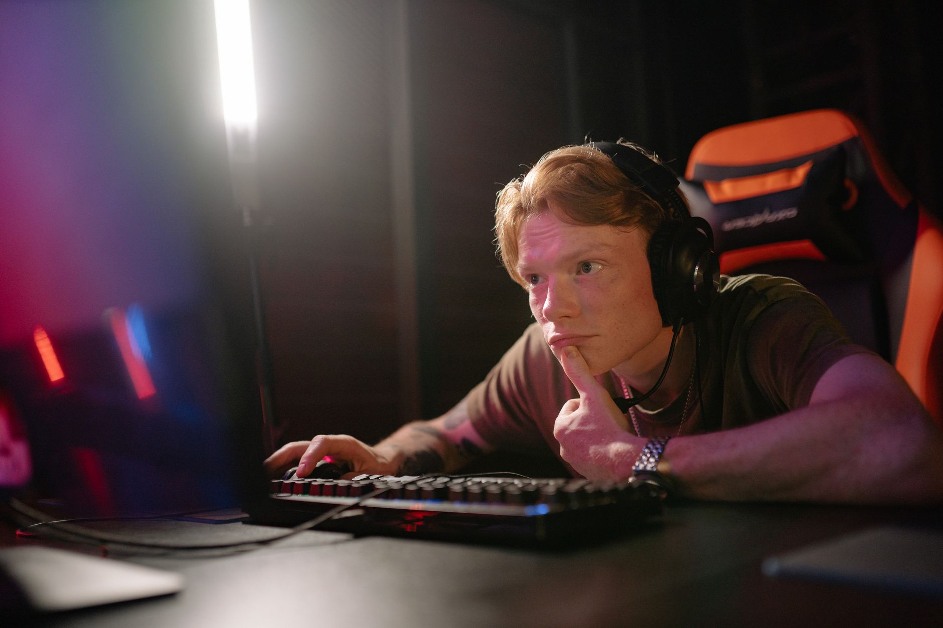 OMS revela o mínimo de atividade física que uma pessoa deve fazer por semana e estudo confirma uma notícia preocupante para os brasileiros 2 Um jovem jogando intensamente em um computador, cercado por equipamentos tecnológicos em uma sala com pouca luz.