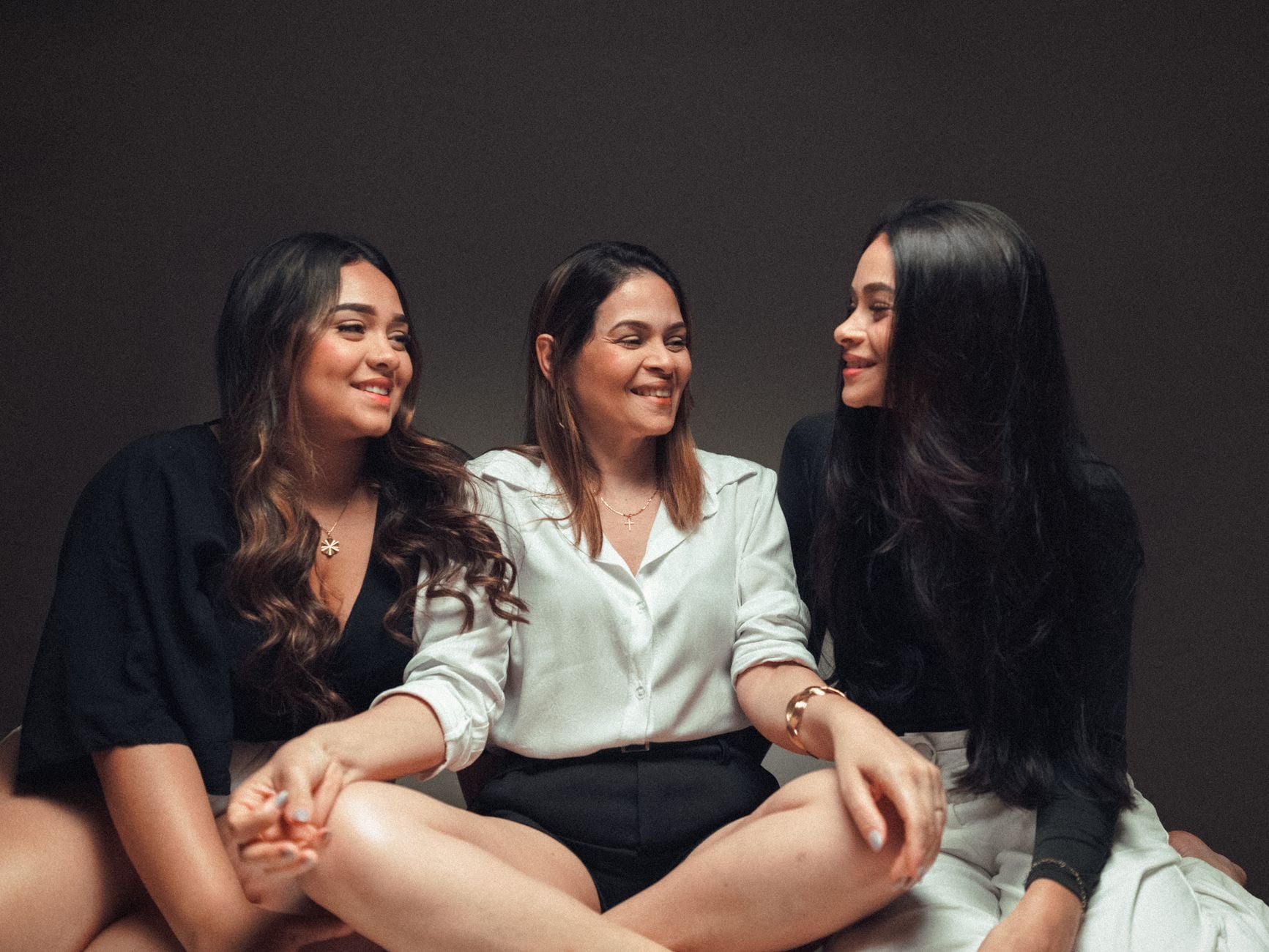 Três mulheres sentadas juntas, sorrindo e desfrutando da companhia uma da outra dentro de casa.