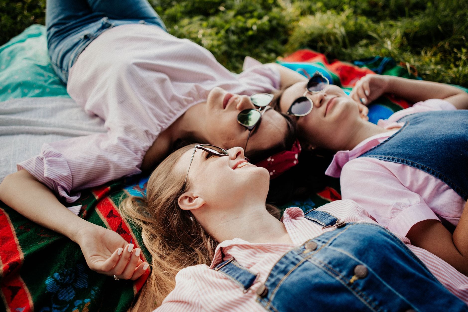 Três mulheres aproveitando um dia ensolarado, relaxando sobre uma toalha de piquenique no parque.