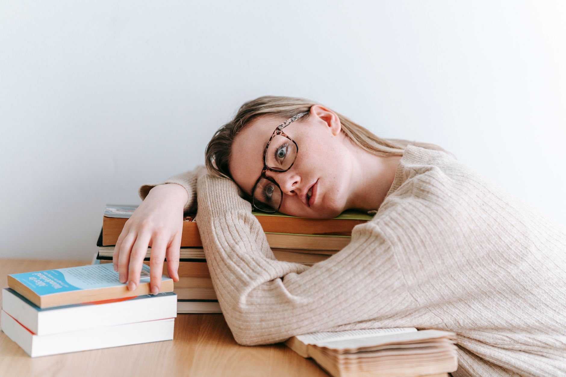 Jovem descansando a cabeça sobre os livros, exemplificando fadiga estudantil e estresse de estudos.