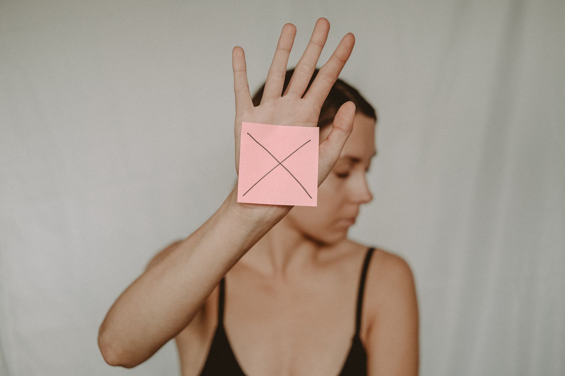 Uma mulher levanta a mão com um papel adesivo rosa exibindo um símbolo de cruz, transmitindo uma mensagem clara de recusa.