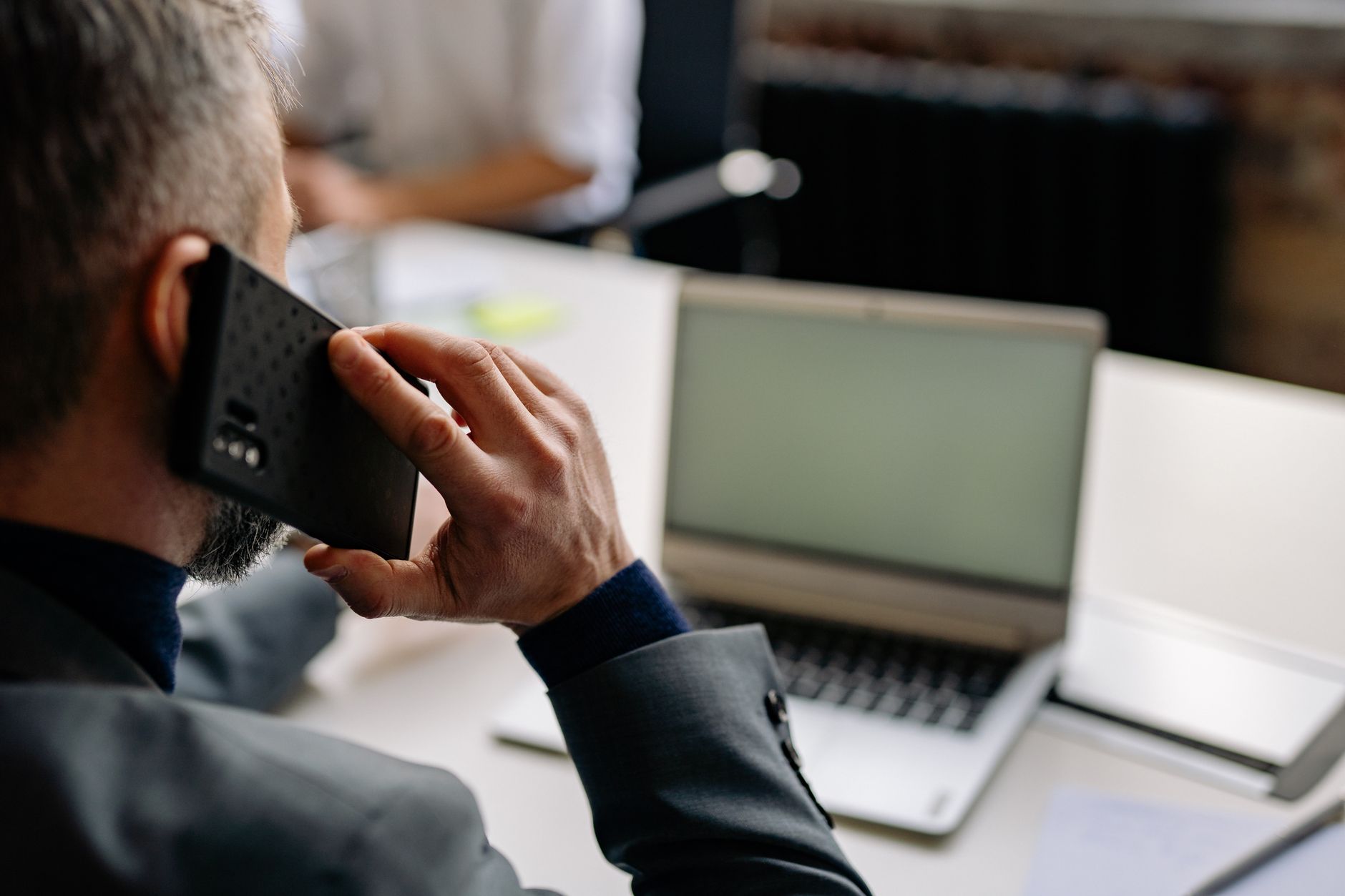 Você deixa o celular tocar e prefere não atender? Psicologia explica por que algumas pessoas ignoram ligações e o que esse comportamento pode revelar 2 Homem profissional utilizando celular em ambiente de escritório, multitarefas com um laptop.