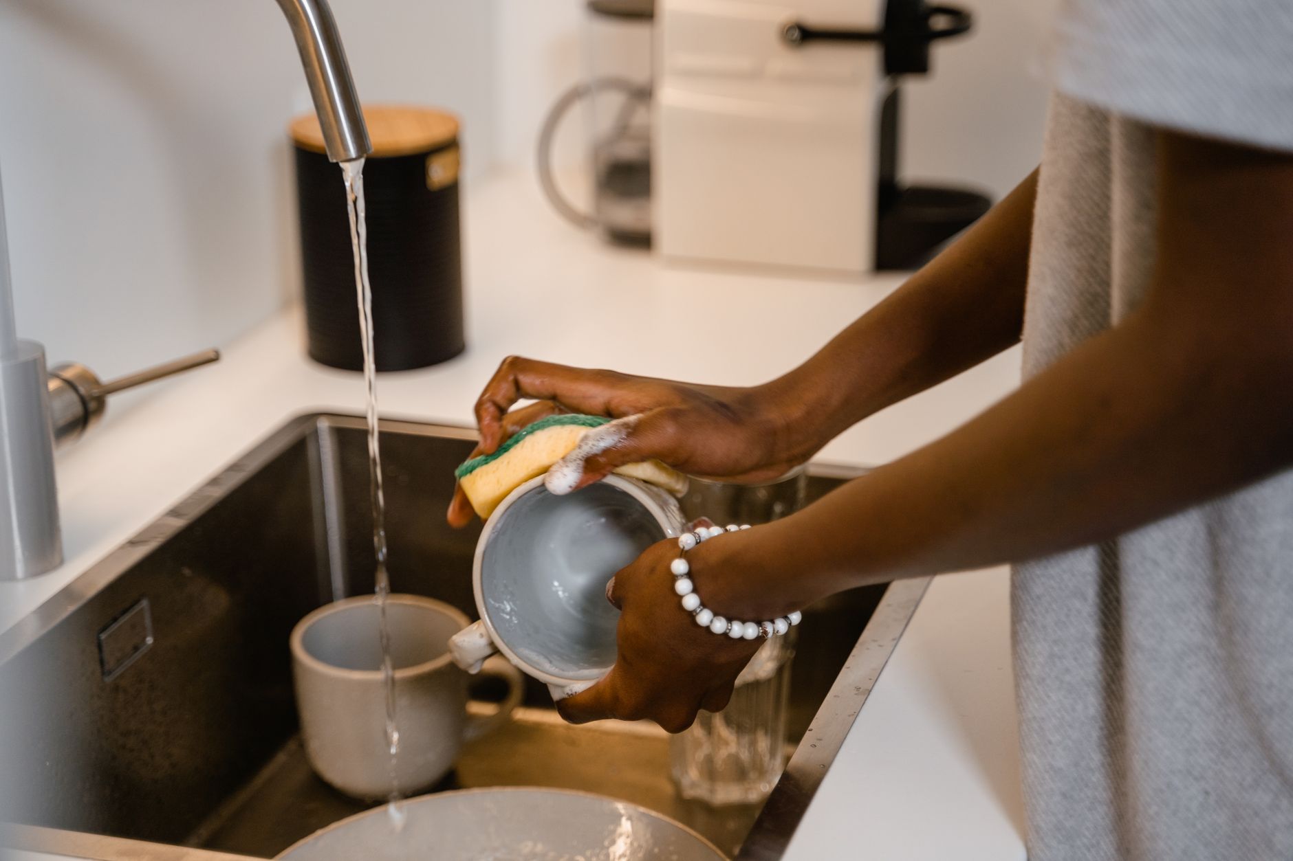 Você enxágua a louça antes de colocar na máquina? Psicologia explica por que tantas pessoas repetem esse hábito mesmo sem precisar 1 Close-up de mulher lavando pratos na pia da cozinha, destacando as mãos com a pulseira.
