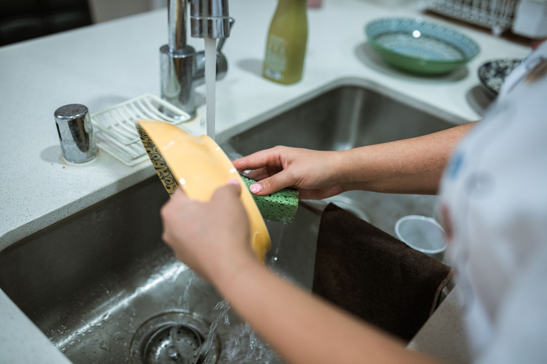 Você enxágua a louça antes de colocar na máquina? Psicologia explica por que tantas pessoas repetem esse hábito mesmo sem precisar 2 Close-up de mãos lavando louças na pia da cozinha com água corrente.