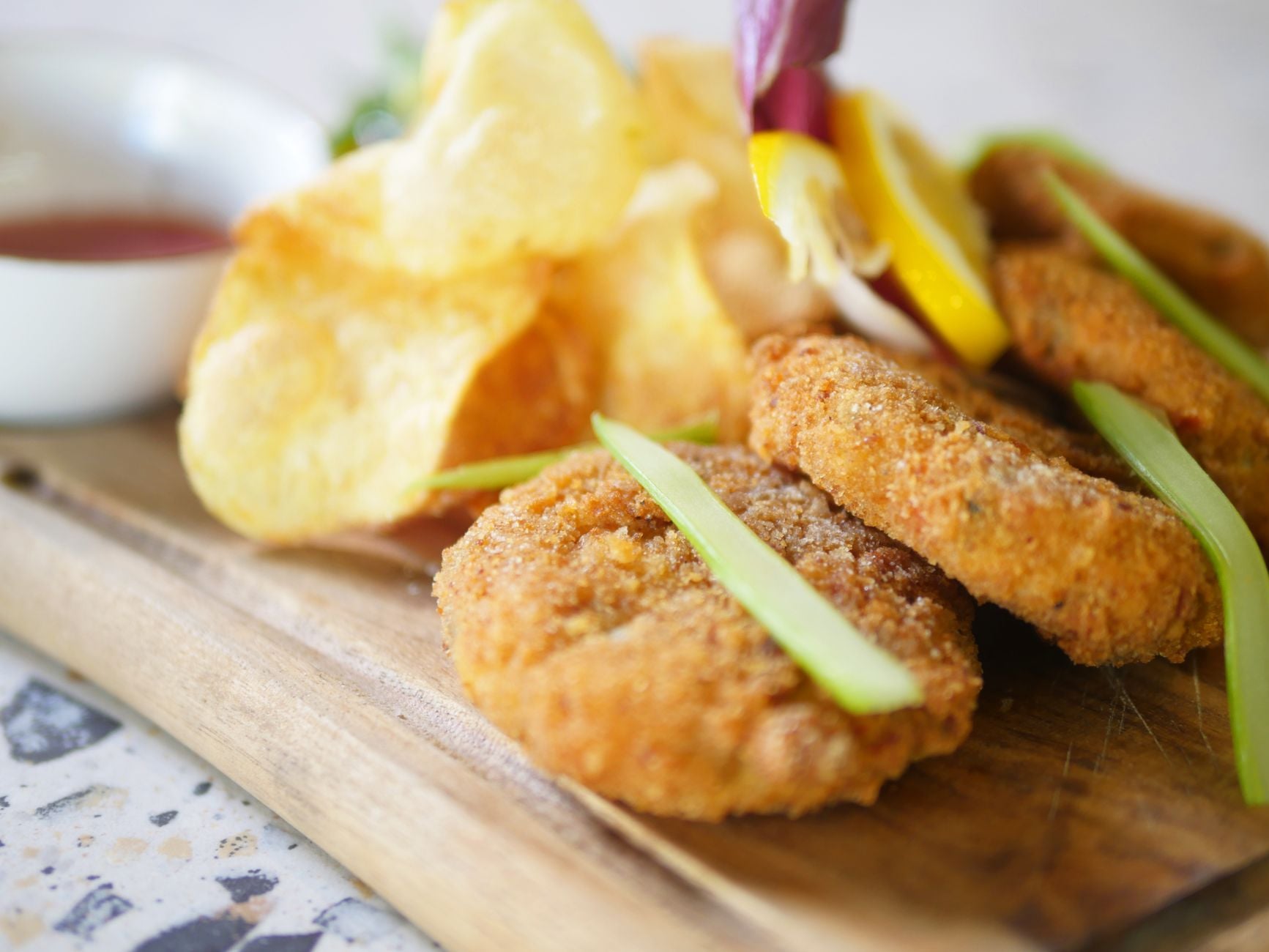 Close-up de deliciosos bolinhos de peixe fritos com batatas fritas em uma tábua de madeira, perfeito para uma refeição saborosa.