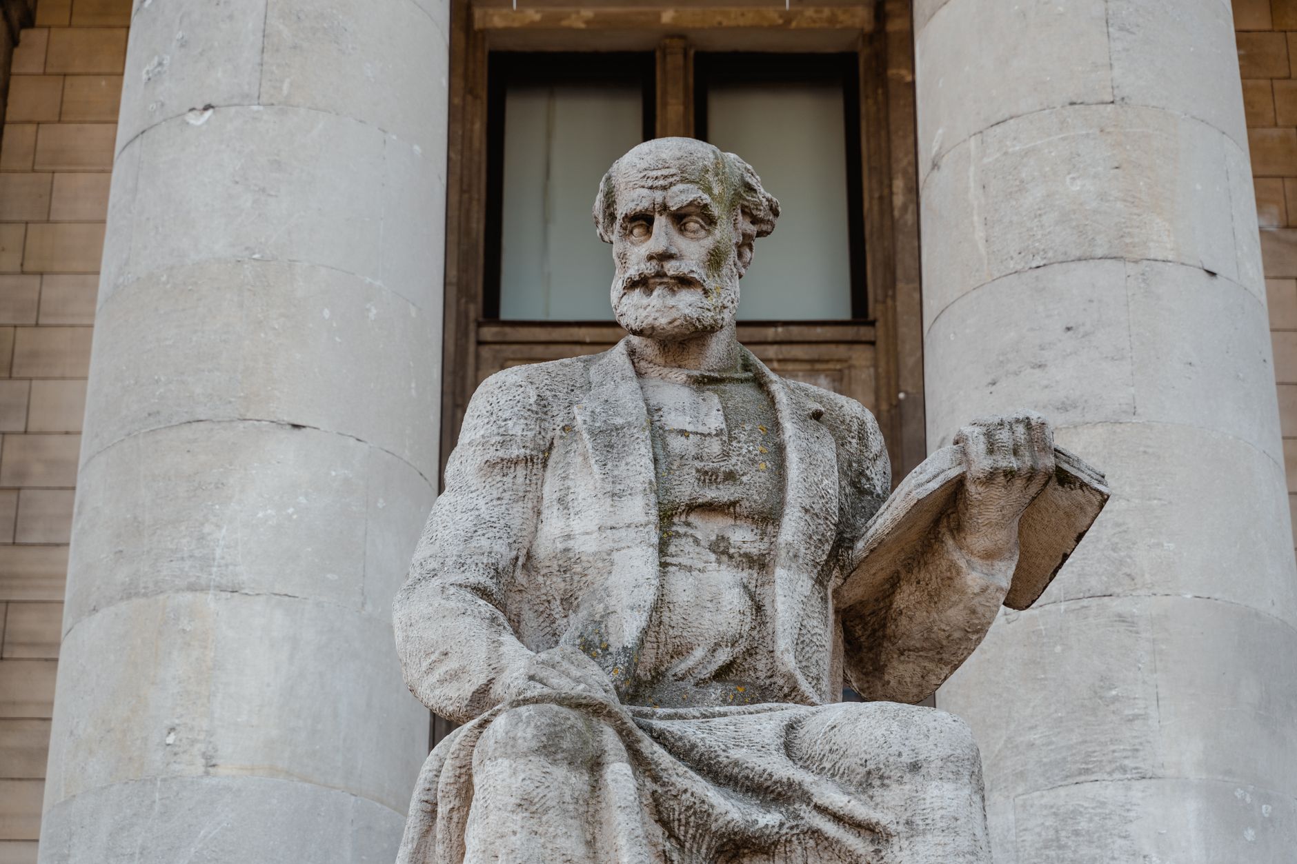 Aristóteles: A democracia surgiu quando, devido ao fato de que todos são iguais em certo sentido, acreditou-se que todos fossem absolutamente iguais entre si 1 Um close-up de uma estátua de pedra histórica com colunas arquitetônicas clássicas em um ambiente urbano.