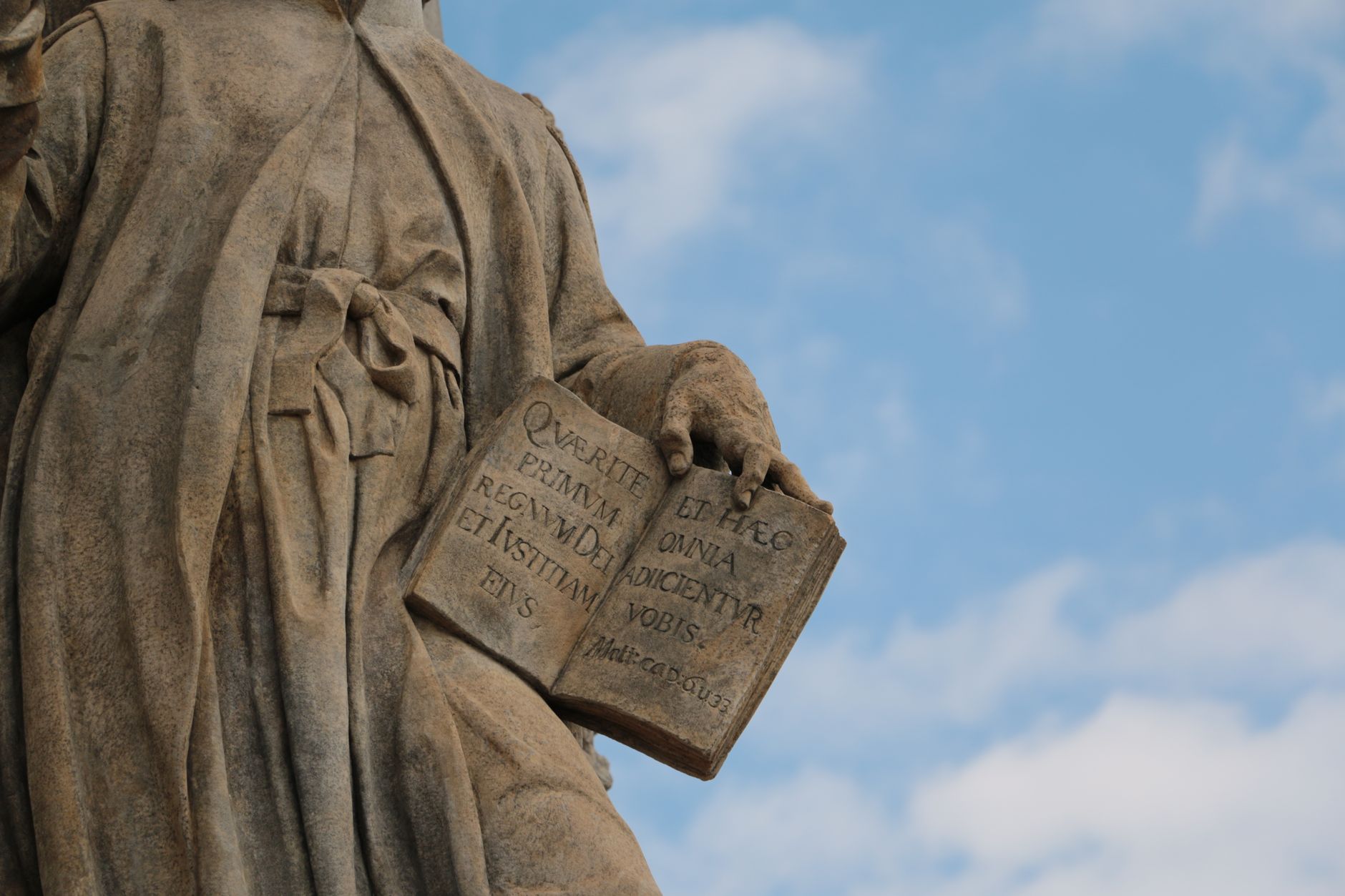 Aristóteles: A democracia surgiu quando, devido ao fato de que todos são iguais em certo sentido, acreditou-se que todos fossem absolutamente iguais entre si 2 Close-up de uma estátua histórica em pedra segurando um livro aberto contra o céu azul.