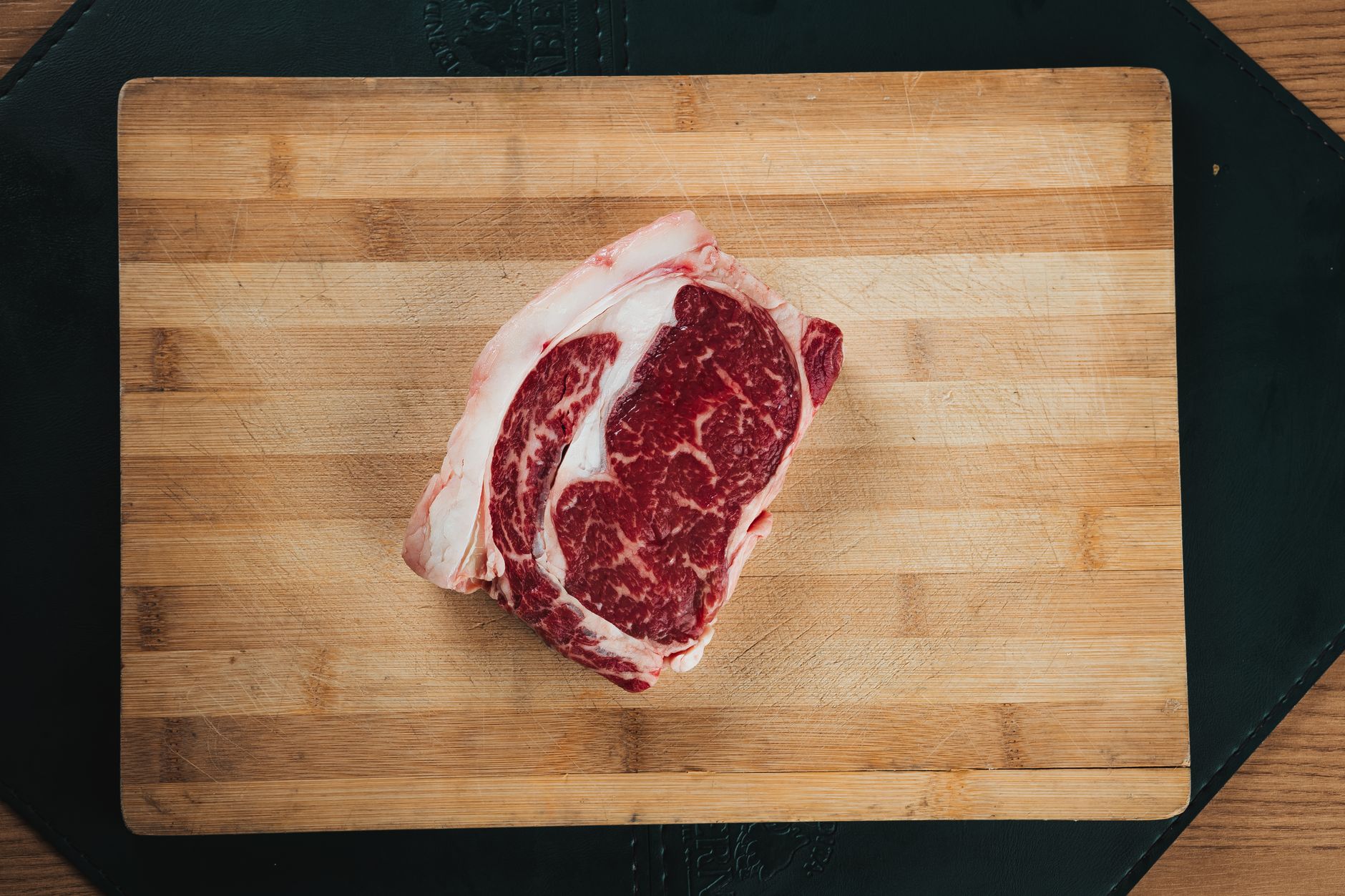Chef revela qual corte de carne é o melhor para quem nunca preparou um bife em casa e explica por que ele é mais fácil de acertar mesmo quando a pessoa ainda não domina o ponto 1 Close-up de um bife ancho marmorizado em uma tábua de corte de madeira, ideal para cozimento e apresentações de alimentos.