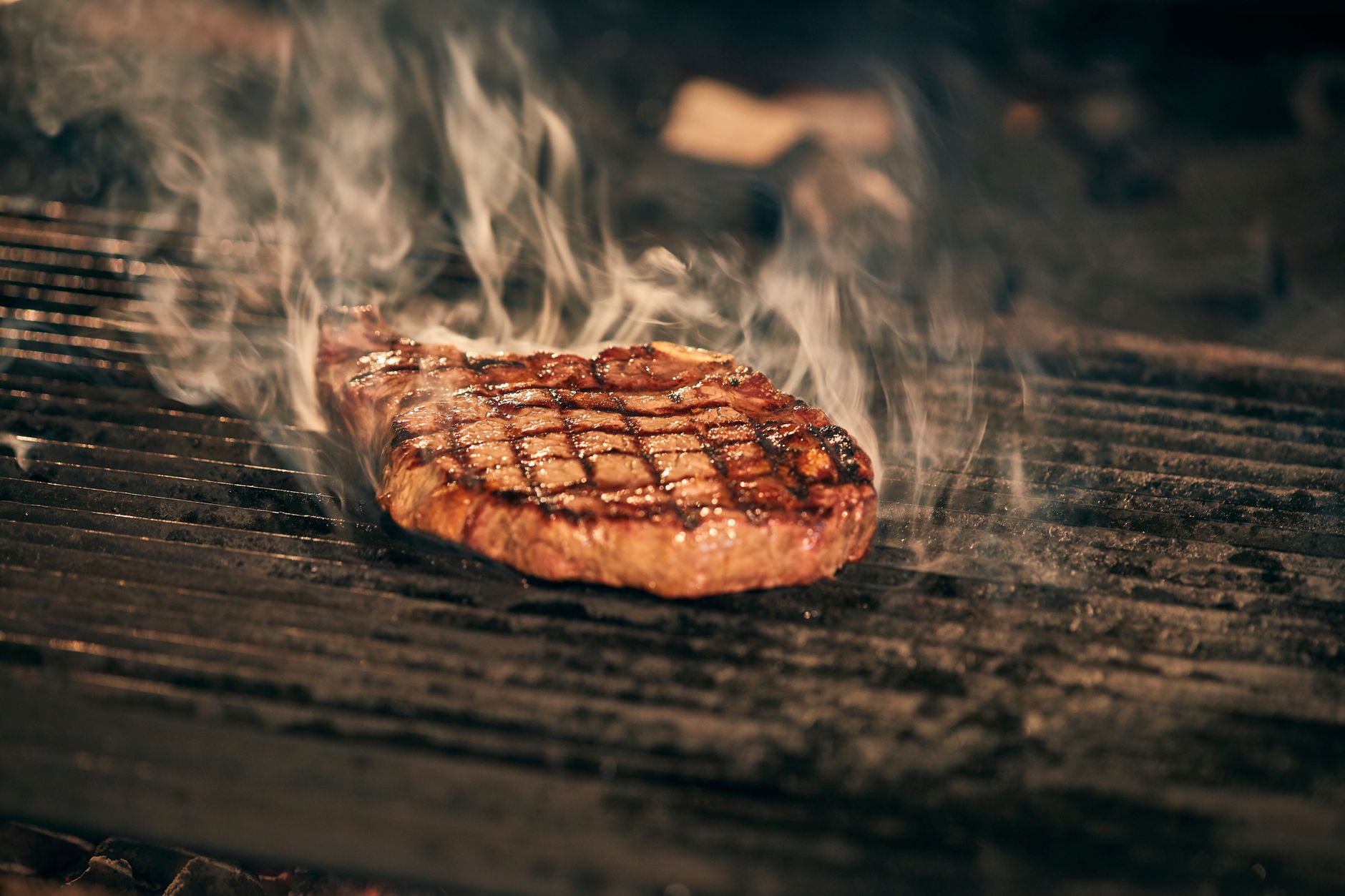 Chef revela qual corte de carne é o melhor para quem nunca preparou um bife em casa e explica por que ele é mais fácil de acertar mesmo quando a pessoa ainda não domina o ponto 2 Close-up de um bife suculento crepitando na churrasqueira com fumaça subindo, capturando a essência de um churrasco perfeito.