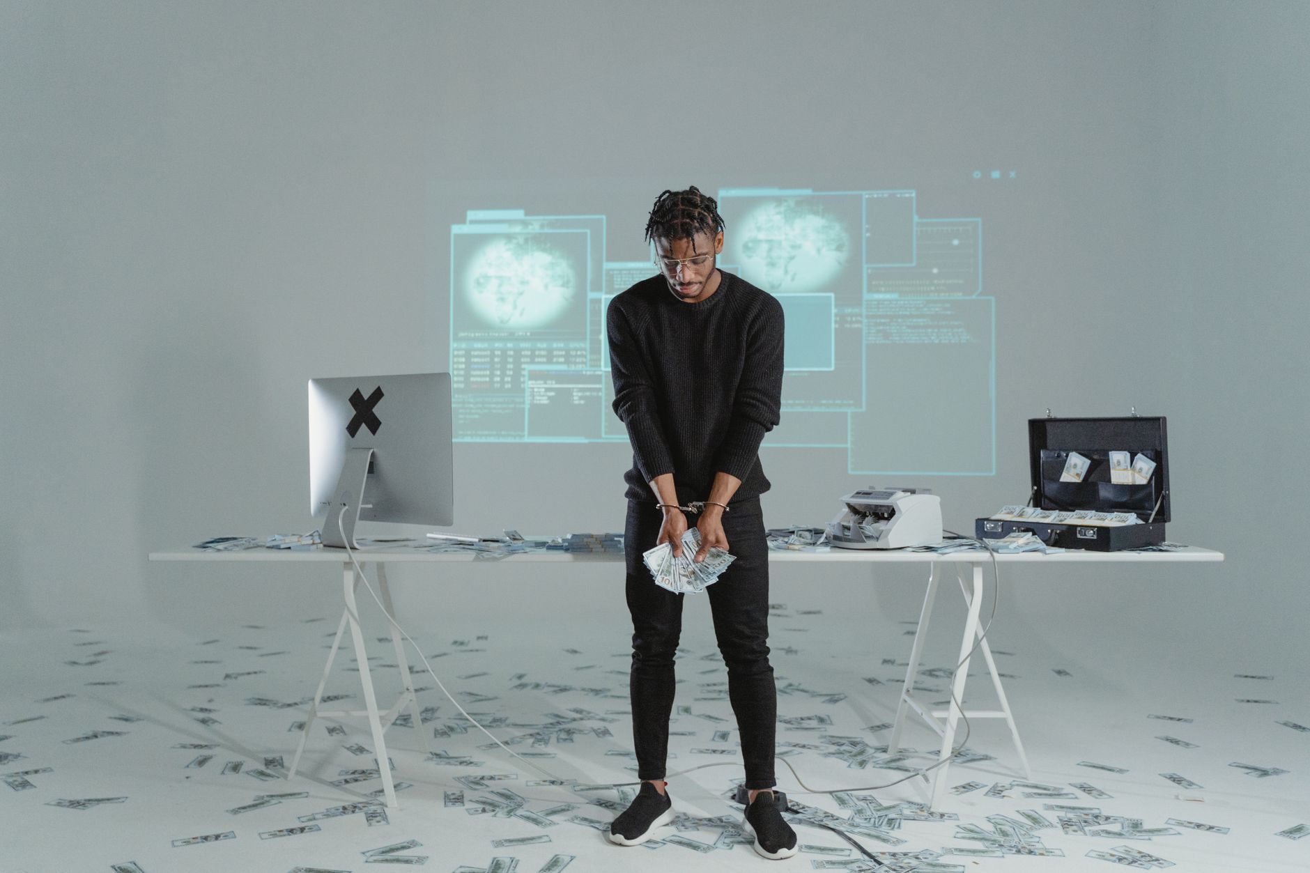 Um homem está segurando dinheiro em uma sala de alta tecnologia com notas espalhadas e um computador.