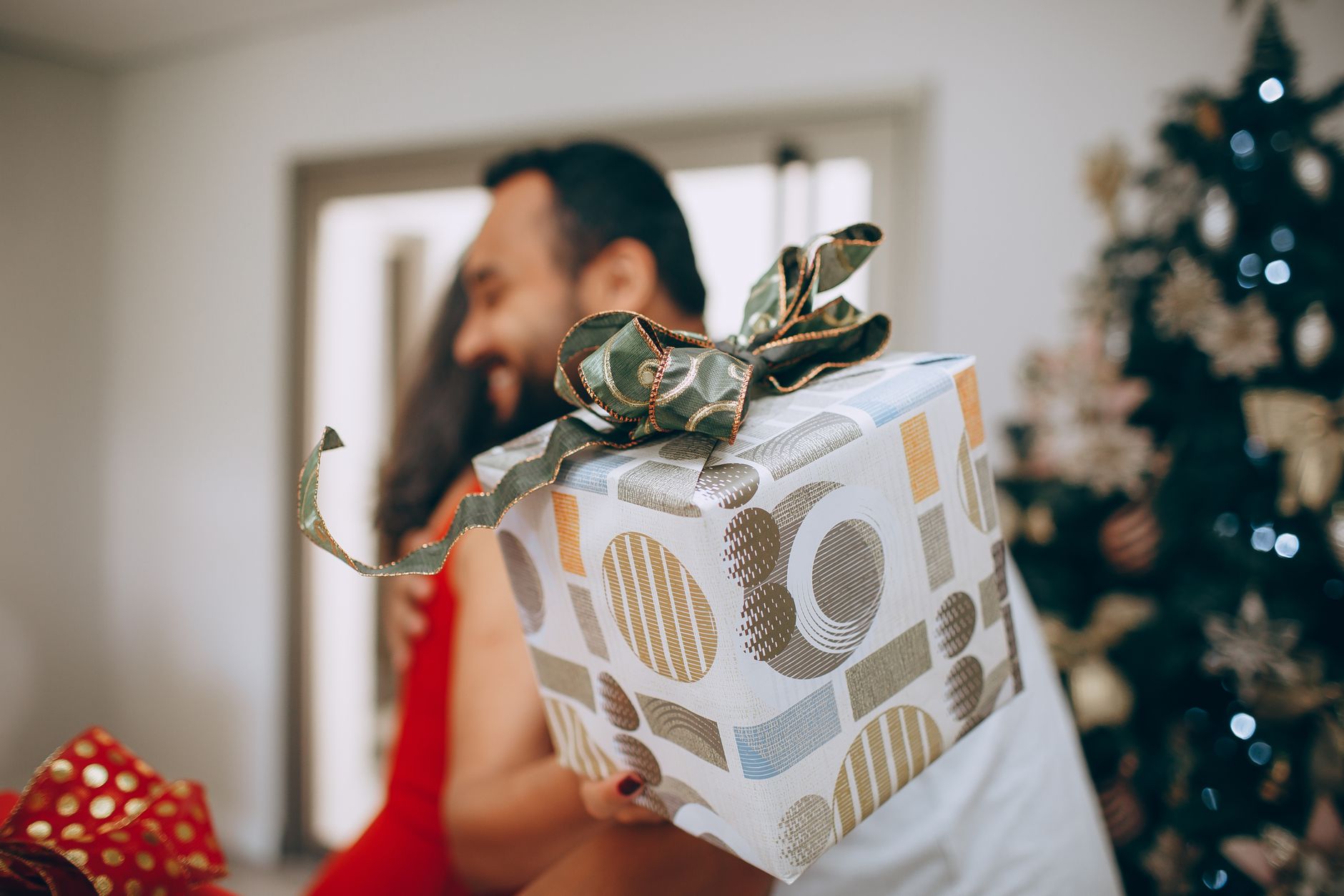 Depois da festa, muita gente simplesmente vai embora, mas especialistas revelam o gesto esquecido que pode fazer o anfitrião lembrar de você de uma forma especial 1 Um casal feliz trocando presentes ao lado de uma árvore de Natal decorada dentro de casa.