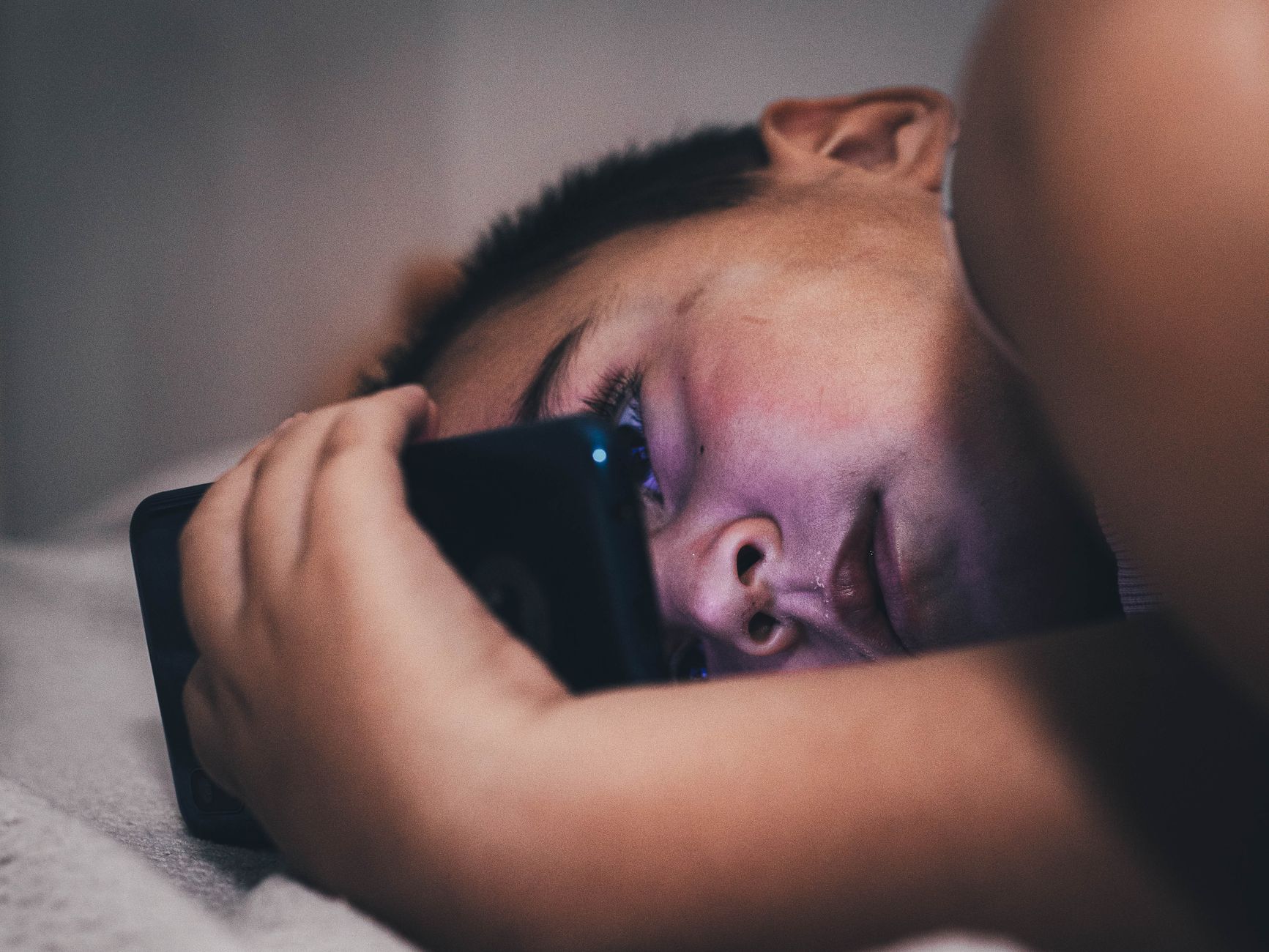 Ele passou anos estudando por que as pessoas dormem mal e descobriu que mudanças simples na rotina podem fazer diferença, incluindo um hábito que muita gente faz antes de deitar 3 Close-up de um adolescente usando um smartphone à noite, criando uma atmosfera sombria.