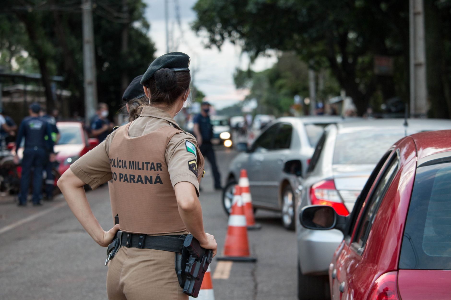 Vista traseira de um policial em uniforme controlando o tráfego em uma estrada movimentada.