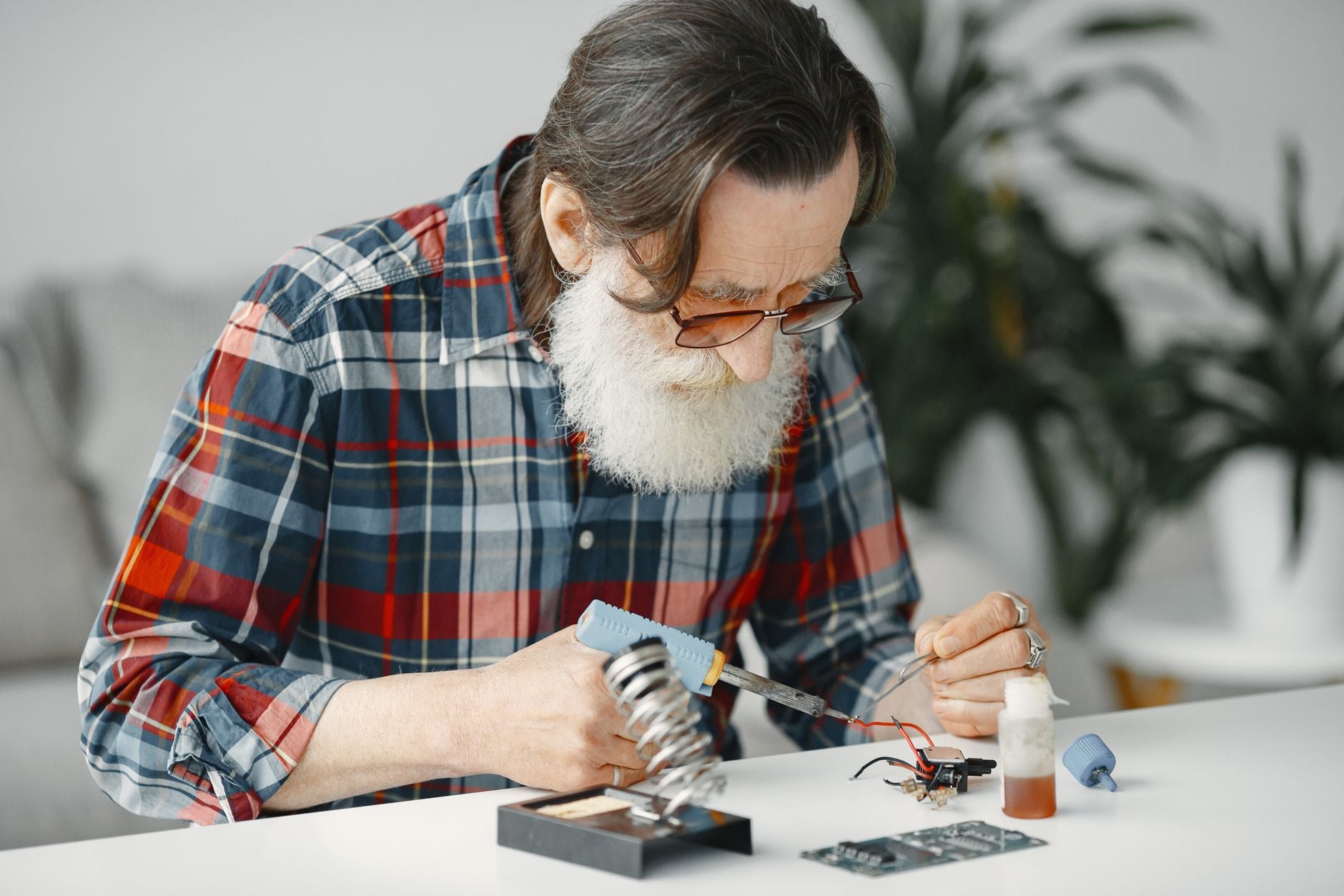Eles não são contra a tecnologia e nem estão presos ao passado: pessoas criadas nos anos 60, 70 e 80 apenas lembram de quando as coisas funcionavam de outra maneira e por isso se recusam a aceitar mudanças que hoje parecem normais 7 Homem idoso soldando componentes eletrônicos, focado em consertos em casa.