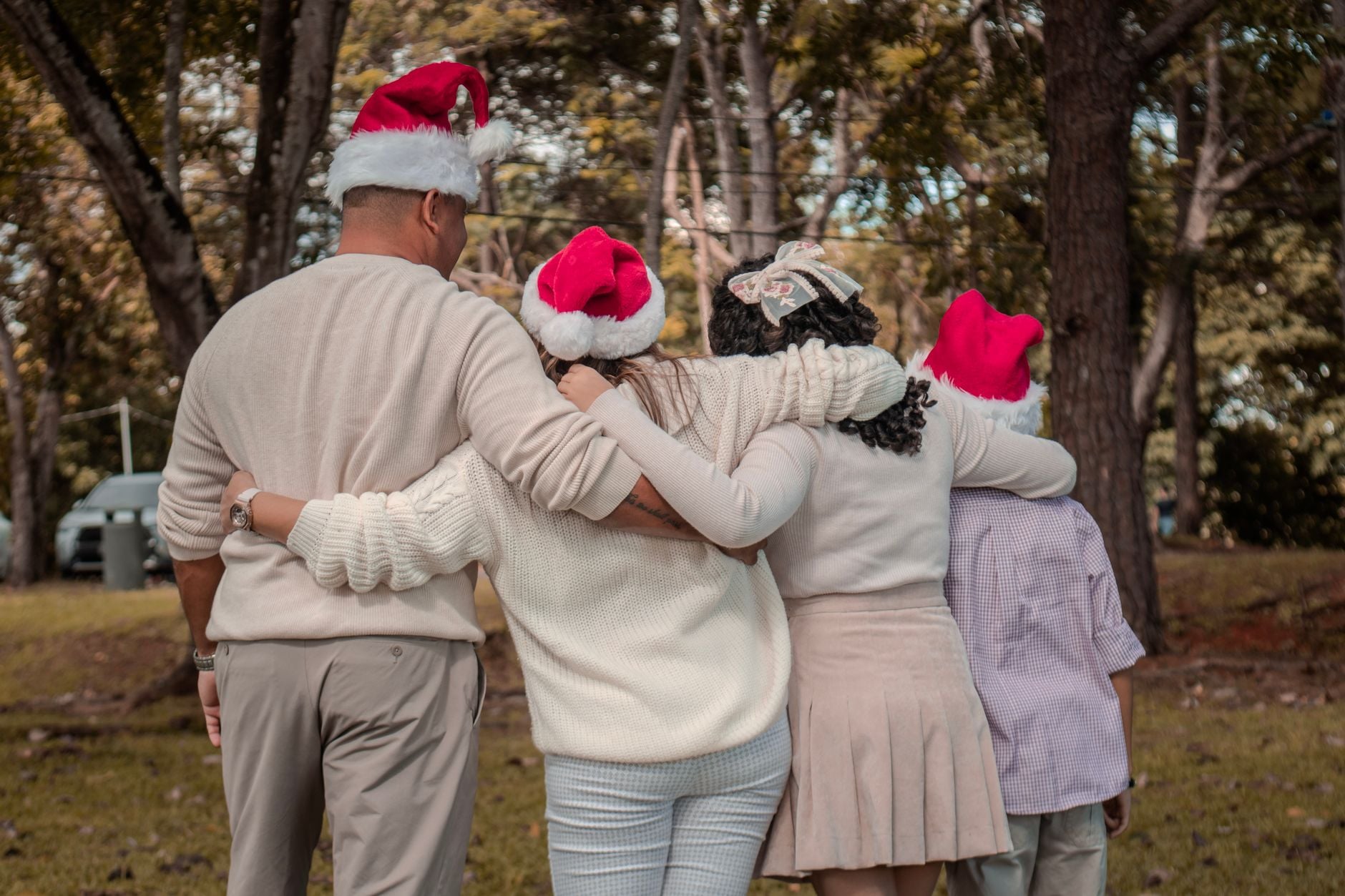 Uma família diversa se abraça ao ar livre com chapéus festivos de Papai Noel, criando uma atmosfera alegre.