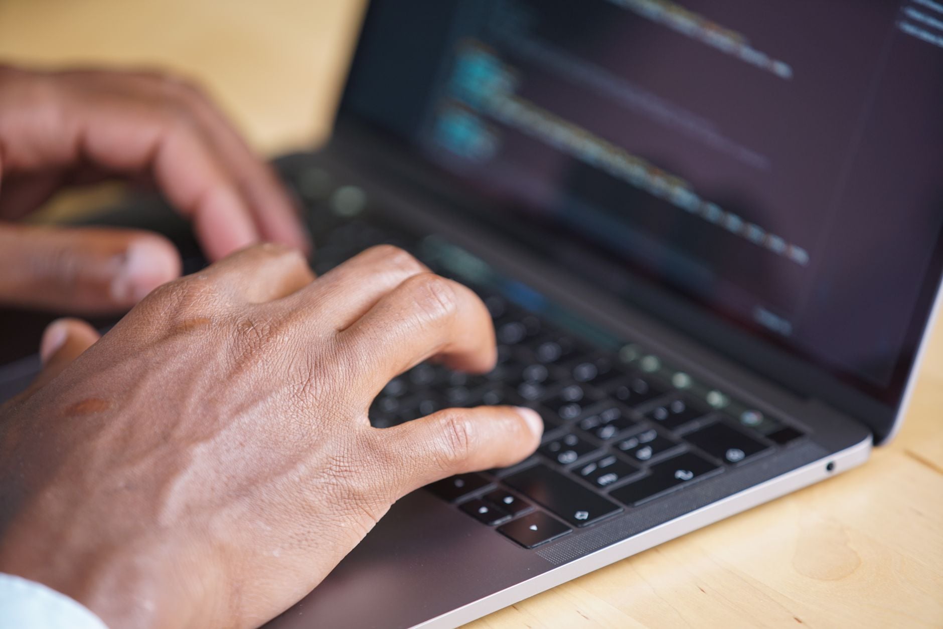 Especialistas revelam o que pode acontecer com o corpo de quem usa computador por mais de 4 horas 2 Mãos digitando em um laptop com código exibido na tela, mostrando o uso da tecnologia.