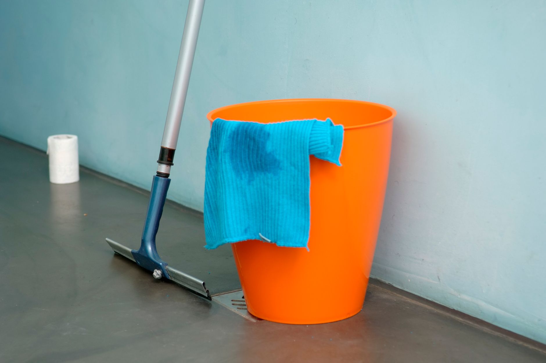 Faxina antes do Natal: a ordem certa para limpar a casa em um dia sem se cansar 4 Close-up de suprimentos de limpeza, incluindo balde laranja, mop e pano azul dentro de casa.