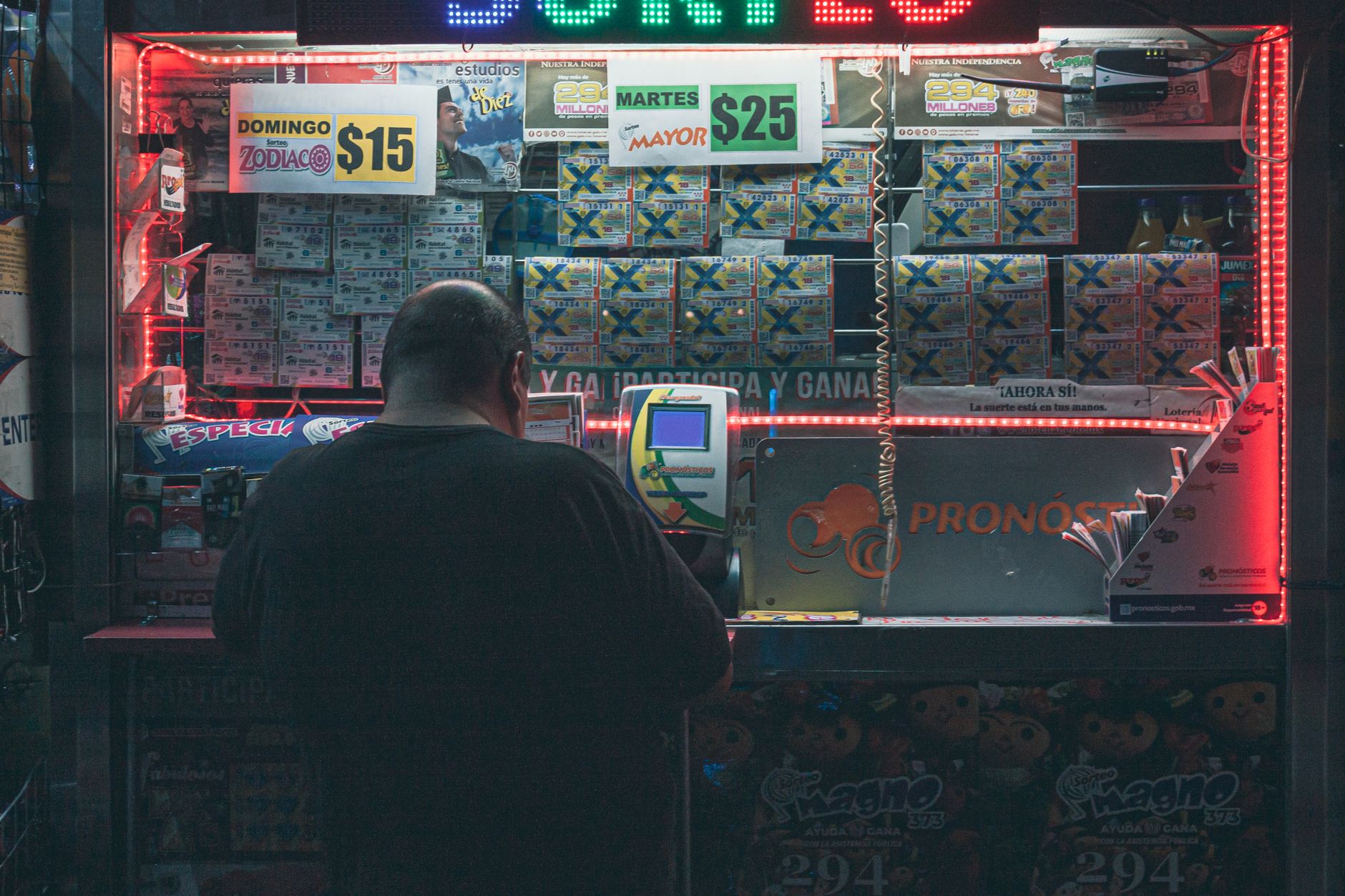 Um homem comprando um bilhete de loteria em um quiosque iluminado na Cidade do México, enfatizando risco e esperança.