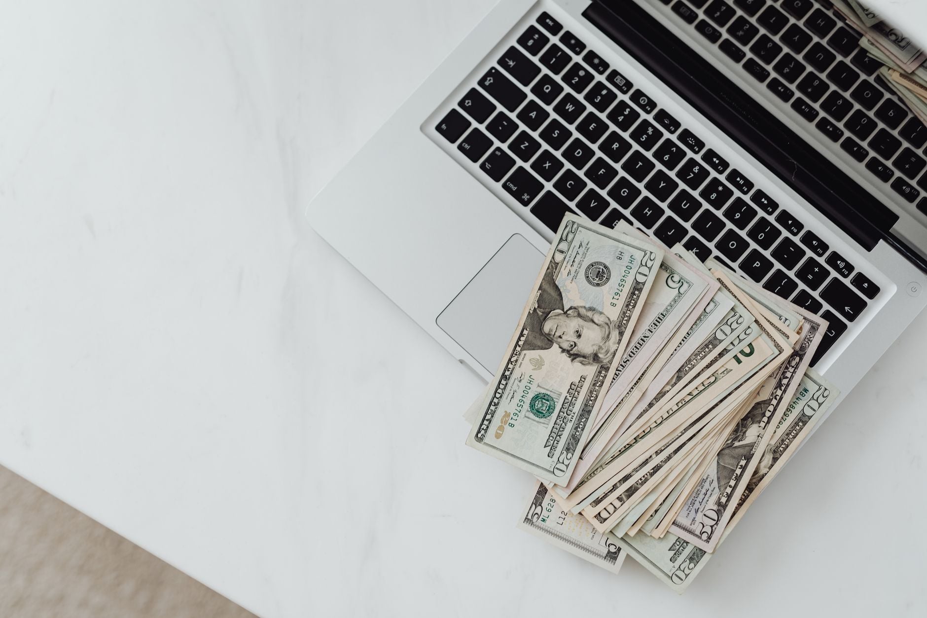 Homem usava relacionamentos iniciados pela internet para convencer mulheres a entregar dinheiro e inventava oportunidades de negócios e investimentos que fizeram as vítimas perderem quase R$ 9,5 milhões 2 Close-up de notas de dólar americano espalhadas sobre o teclado de um notebook em uma mesa branca, simbolizando finanças digitais.