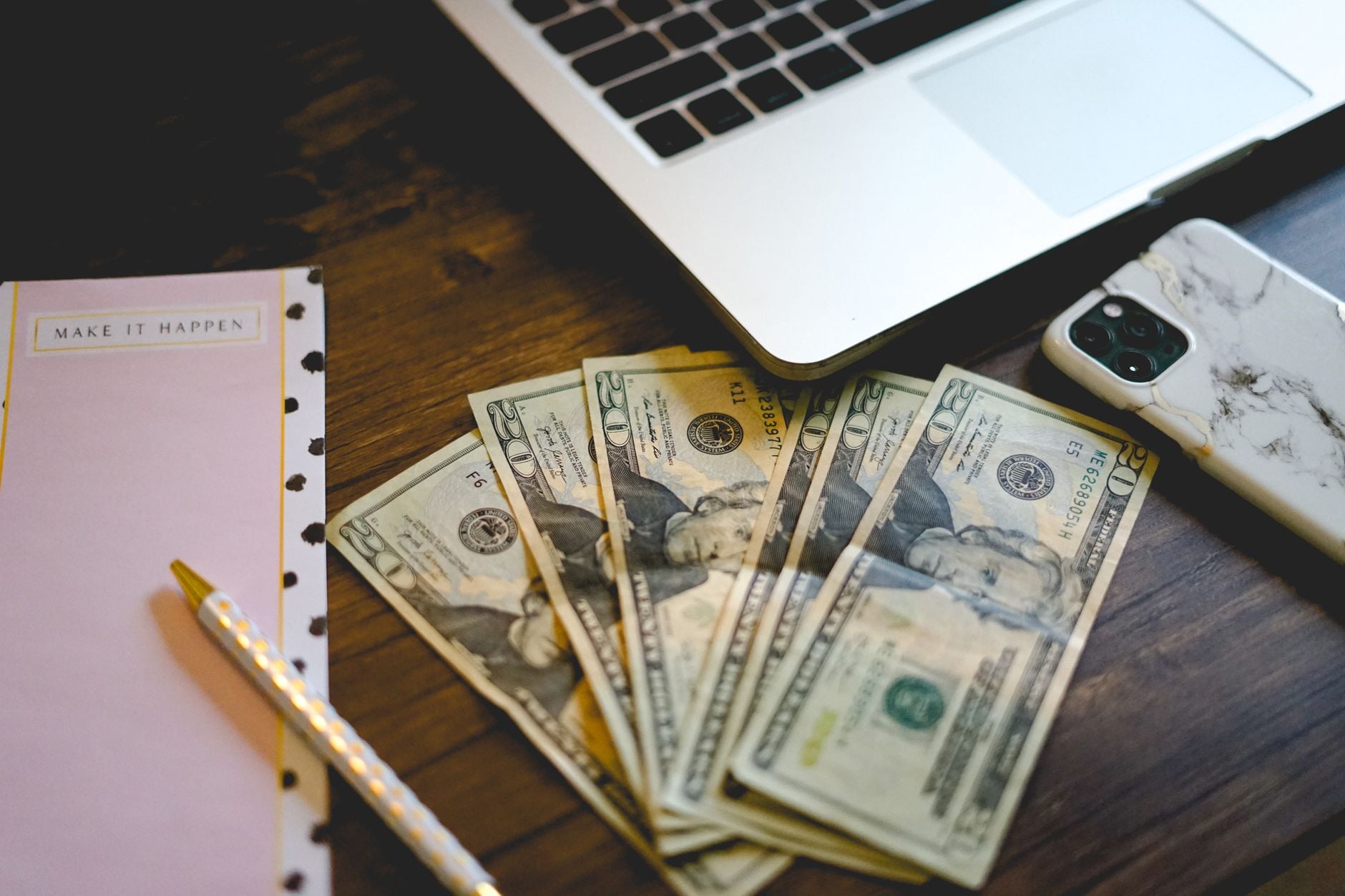 Homem usava relacionamentos iniciados pela internet para convencer mulheres a entregar dinheiro e inventava oportunidades de negócios e investimentos que fizeram as vítimas perderem quase R$ 9,5 milhões 3 Um espaço de trabalho com notas de dólar, bloco de anotações e laptop em uma mesa de madeira.