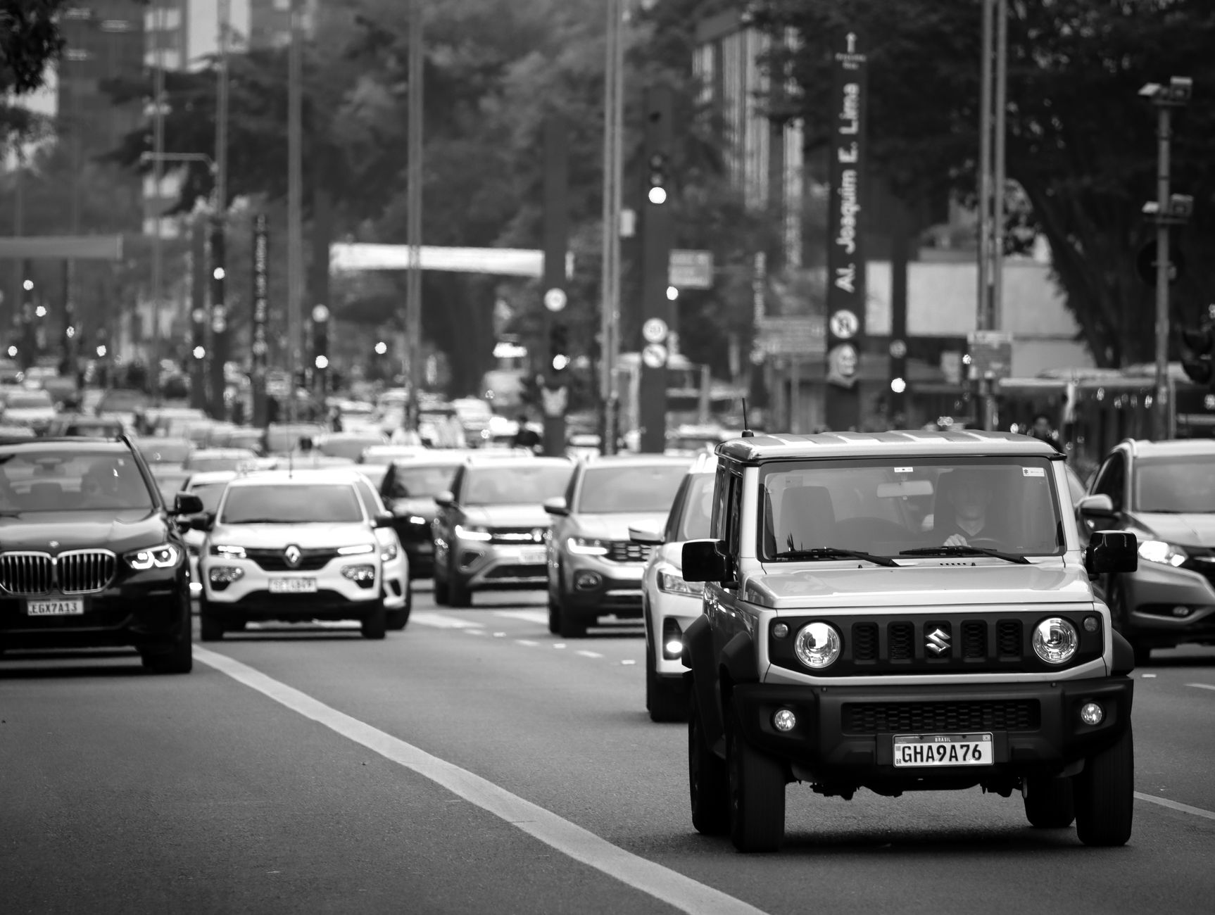Horas no trânsito estão desgastando trabalhadores brasileiros e podem afetar o humor, a saúde e o desempenho profissional 1 Uma cena movimentada de rua na cidade com vários carros em movimento, capturada em preto e branco.
