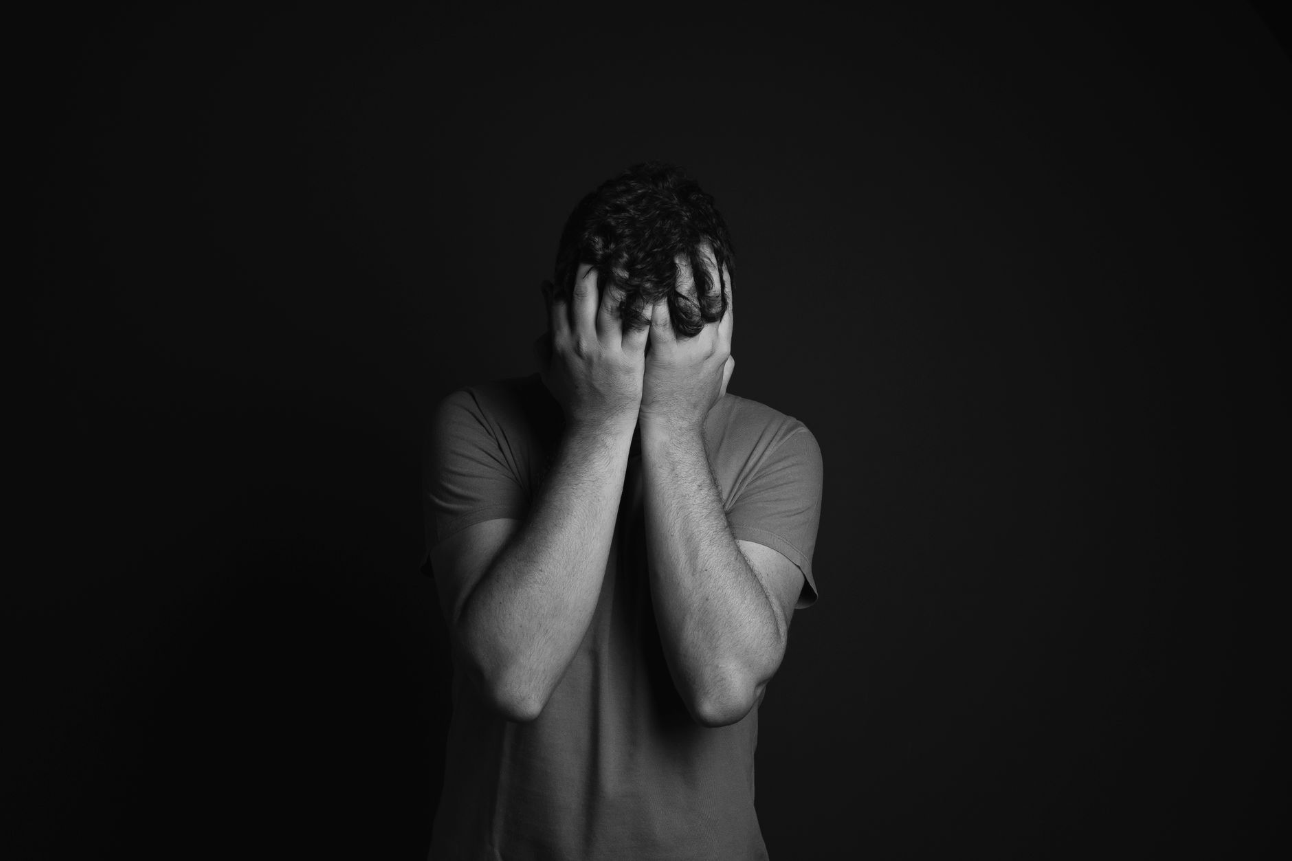 Mesmo sabendo que a morte faz parte da vida, muitas pessoas evitam pensar nela e sentem ansiedade quando o assunto aparece, e a psicologia explica o que realmente está por trás desse medo 2 Um retrato em escala de cinza de um homem cobrindo o rosto, retratando emoções e temas de saúde mental.