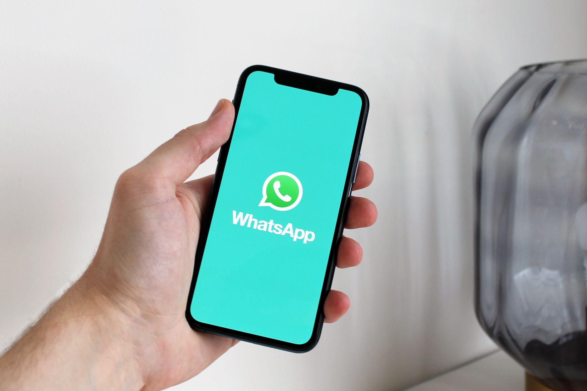Close-up de uma mão segurando um smartphone exibindo a tela do app WhatsApp.