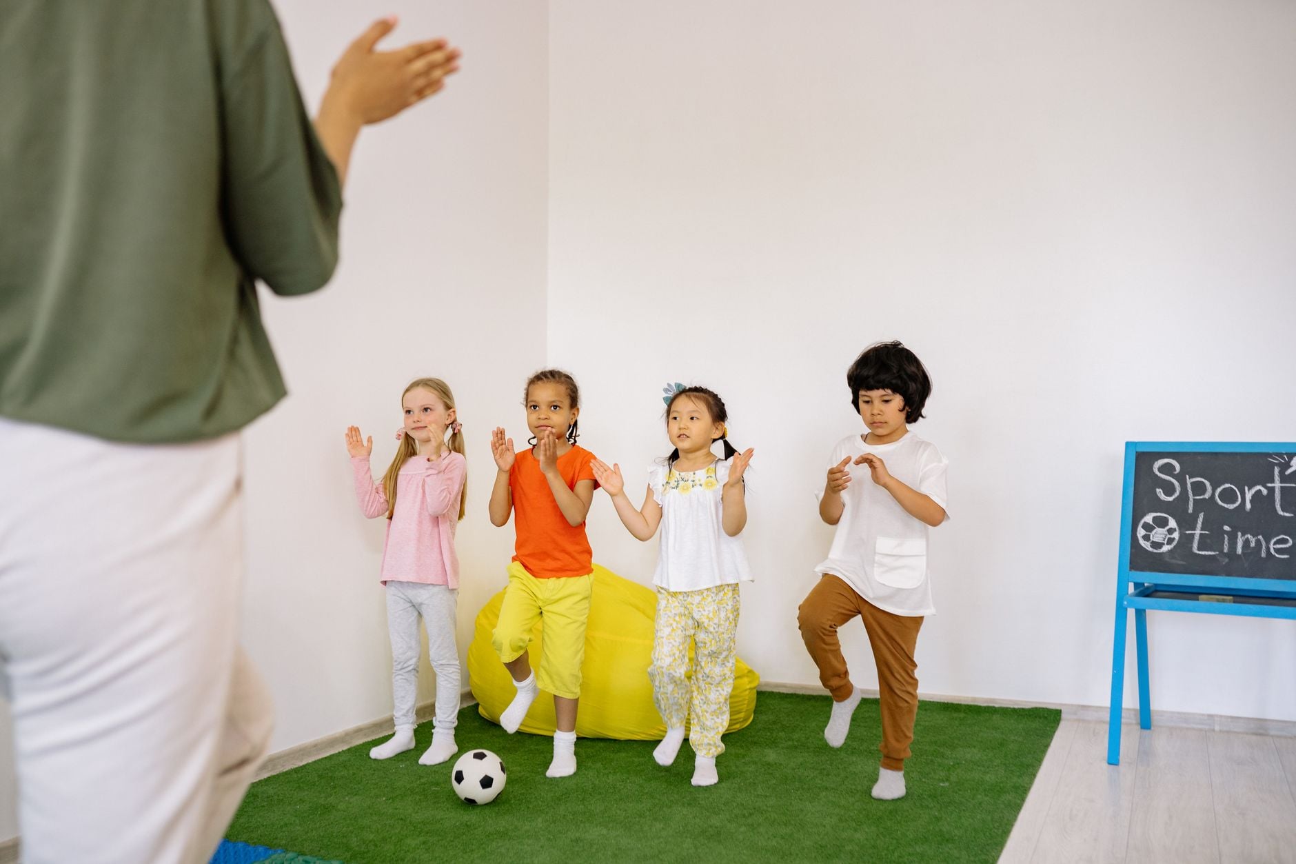 Um grupo de crianças em idade pré-escolar participando de uma divertida atividade esportiva indoor liderada por um professor.